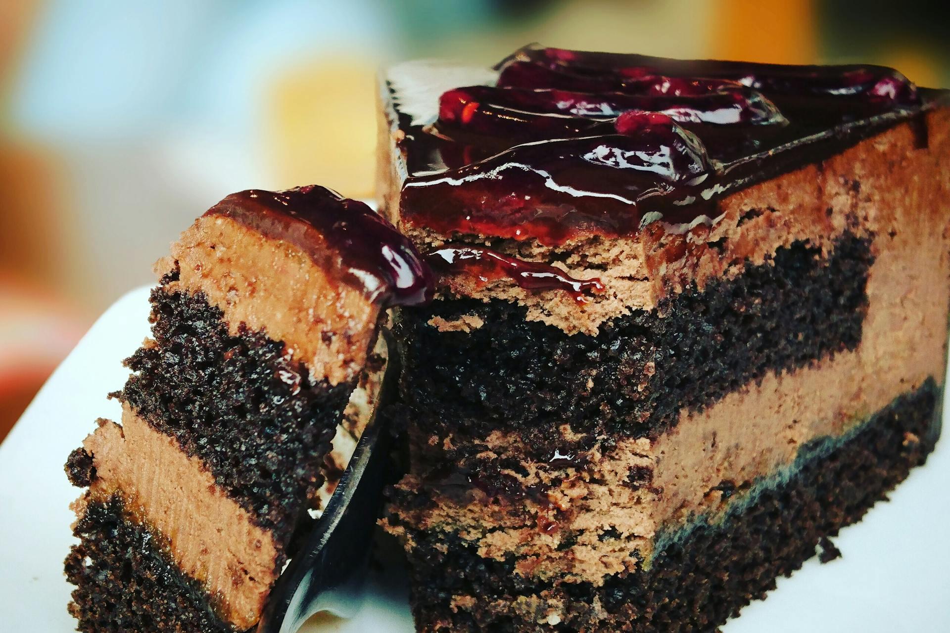 Close-up of a rich chocolate cake slice, layered with creamy mousse and topped with glossy cherry glaze, evoking indulgence and sweetness.