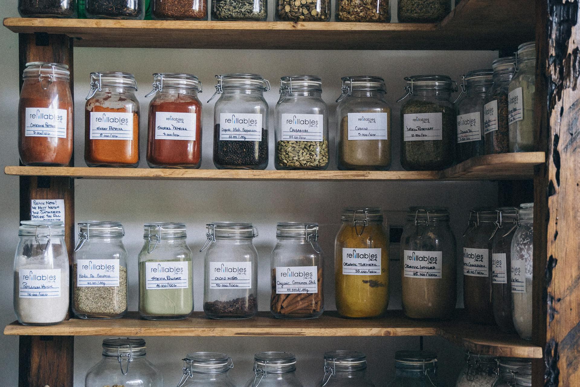 Wooden shelves display various glass jars filled with spices, legumes, and grains. The scene conveys an organized and rustic kitchen vibe.