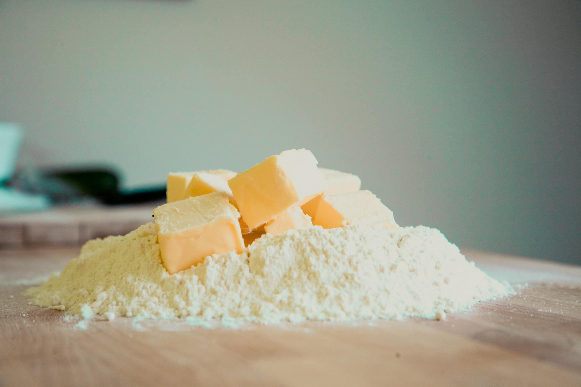A pile of flour with cubes of butter on top sits on a wooden surface, ready for baking.