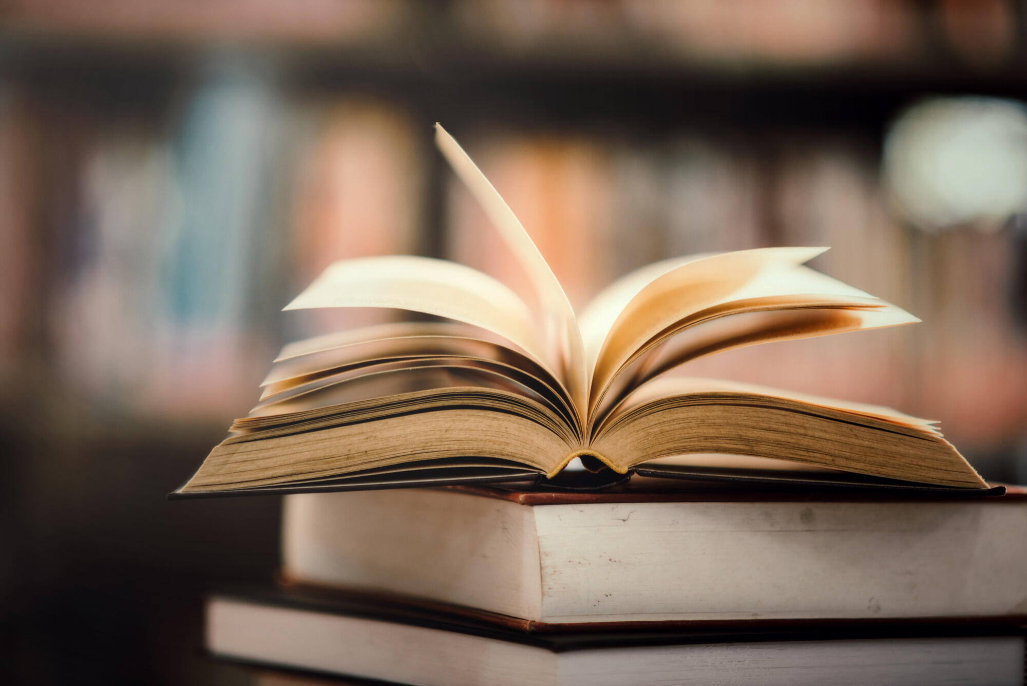 An open book rests on a stack of closed books, showcasing its pages and inviting reading.