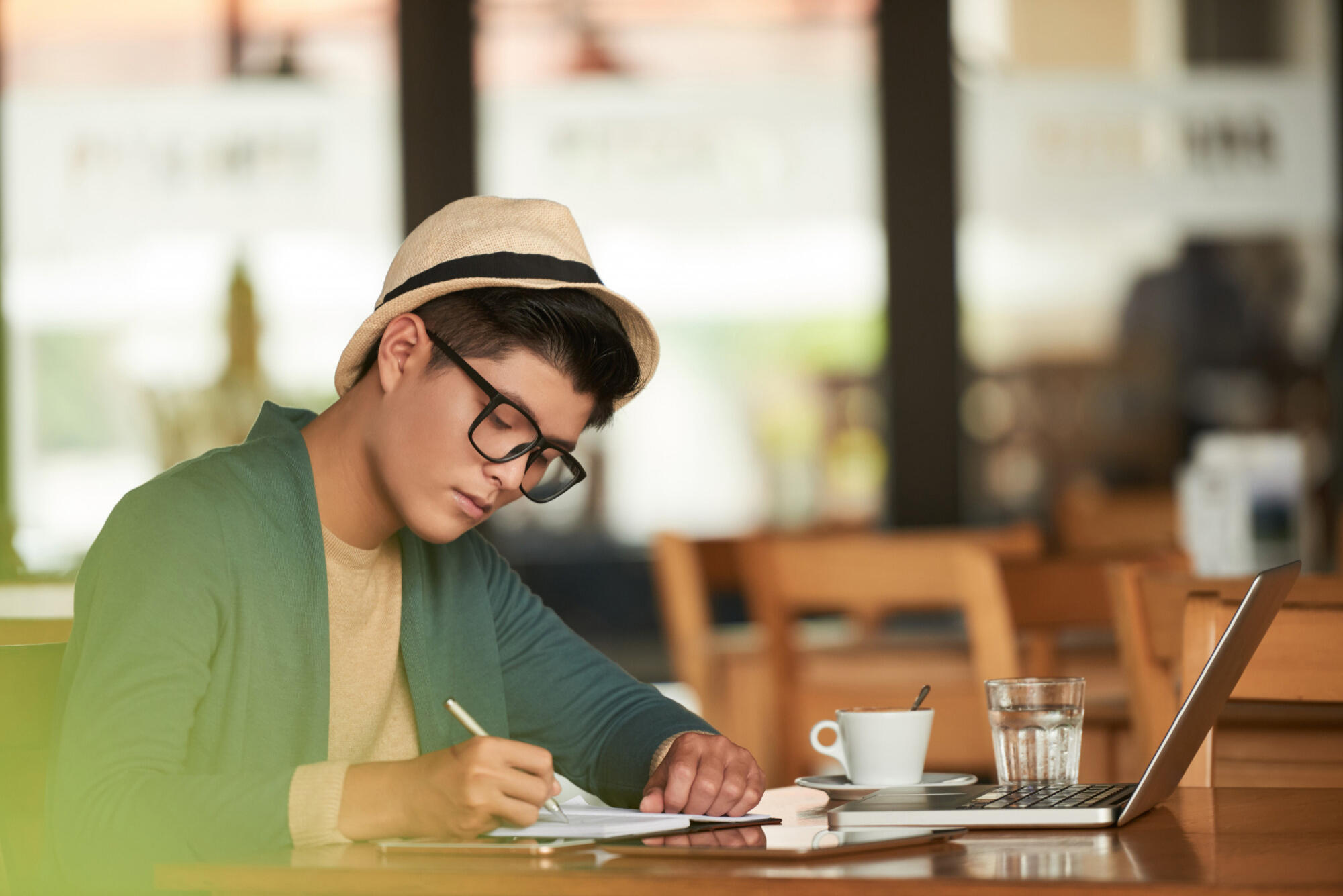 A man in a hat diligently writes on a sheet of paper, showcasing concentration and creativity.