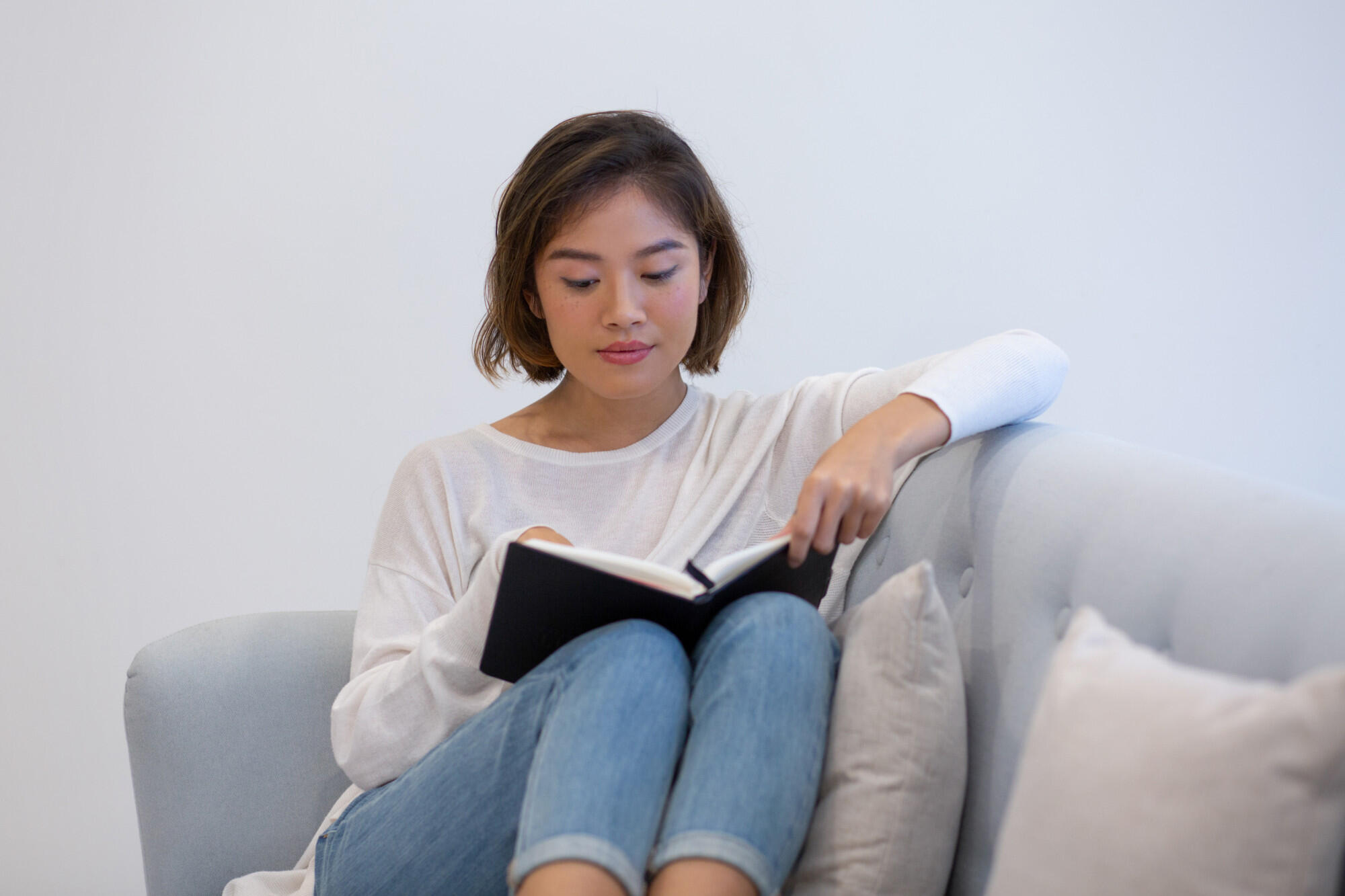 A woman sits on a couch, engrossed in reading a book, with a cozy atmosphere surrounding her.