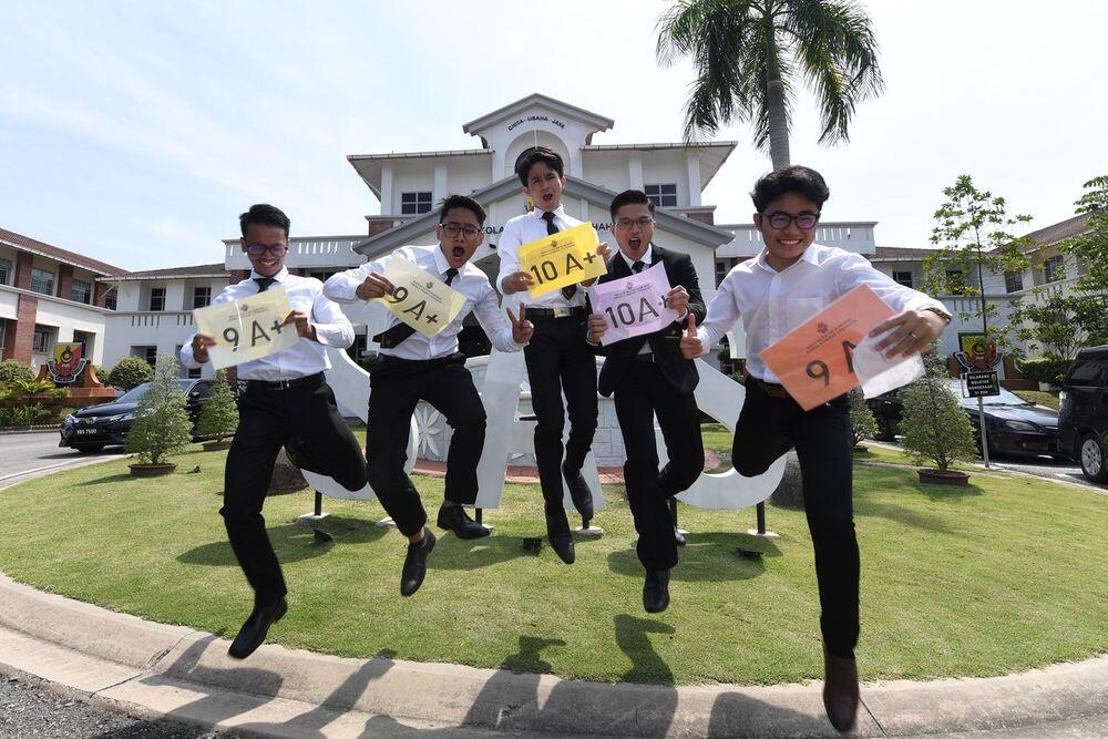 Malaysian students celebrating SPM exam results, jumping while holding grade slips showing multiple A+ score