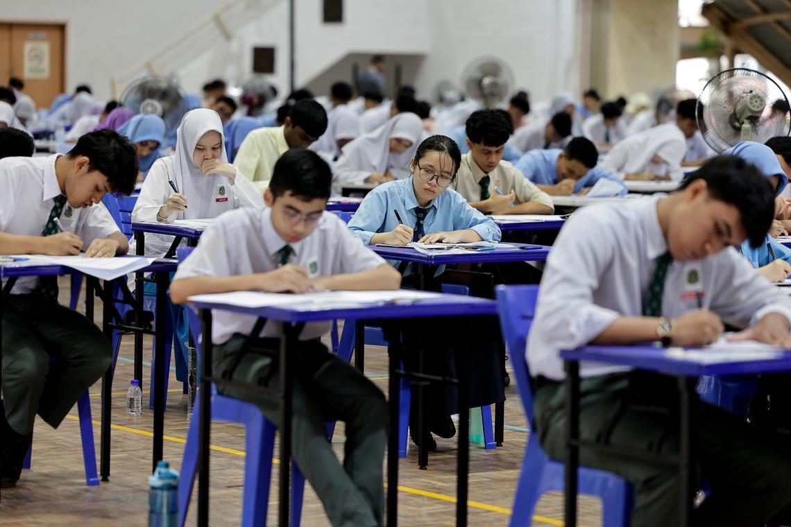 Students taking an exam at blue tables in a large hall