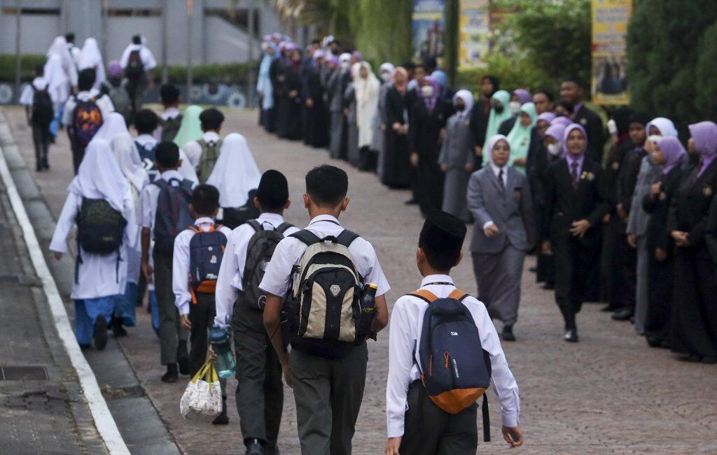 Malaysian students in school uniforms walking toward a school assembly or gathering in the courtyard