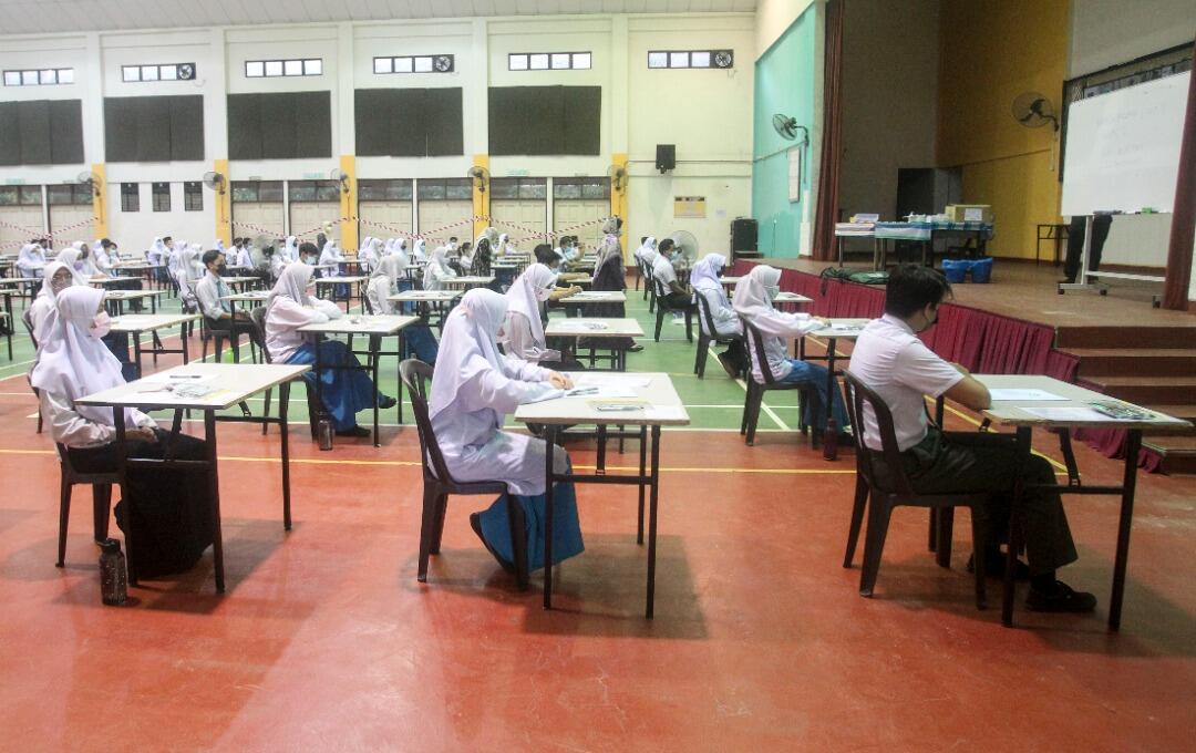 Students taking an exam in a large hall with individual desks