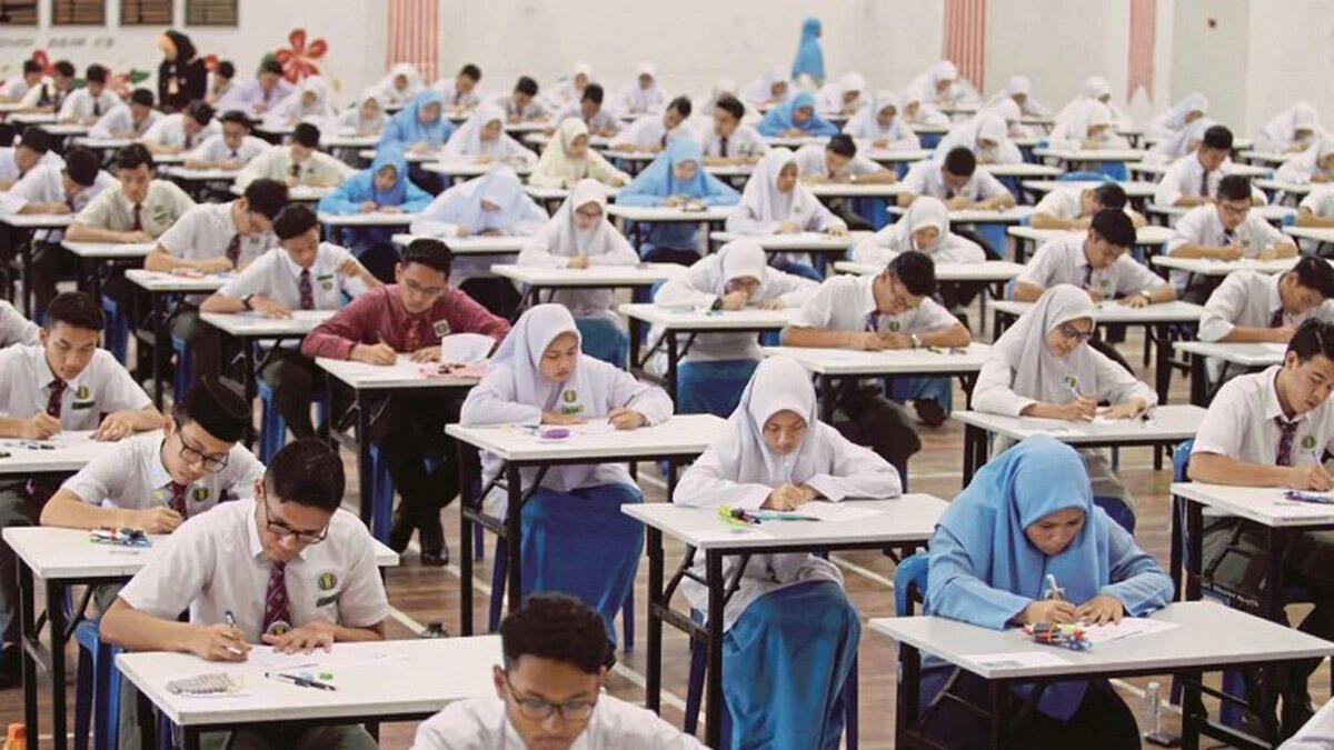 tudents in school uniforms taking an exam at individual desks in a large hall