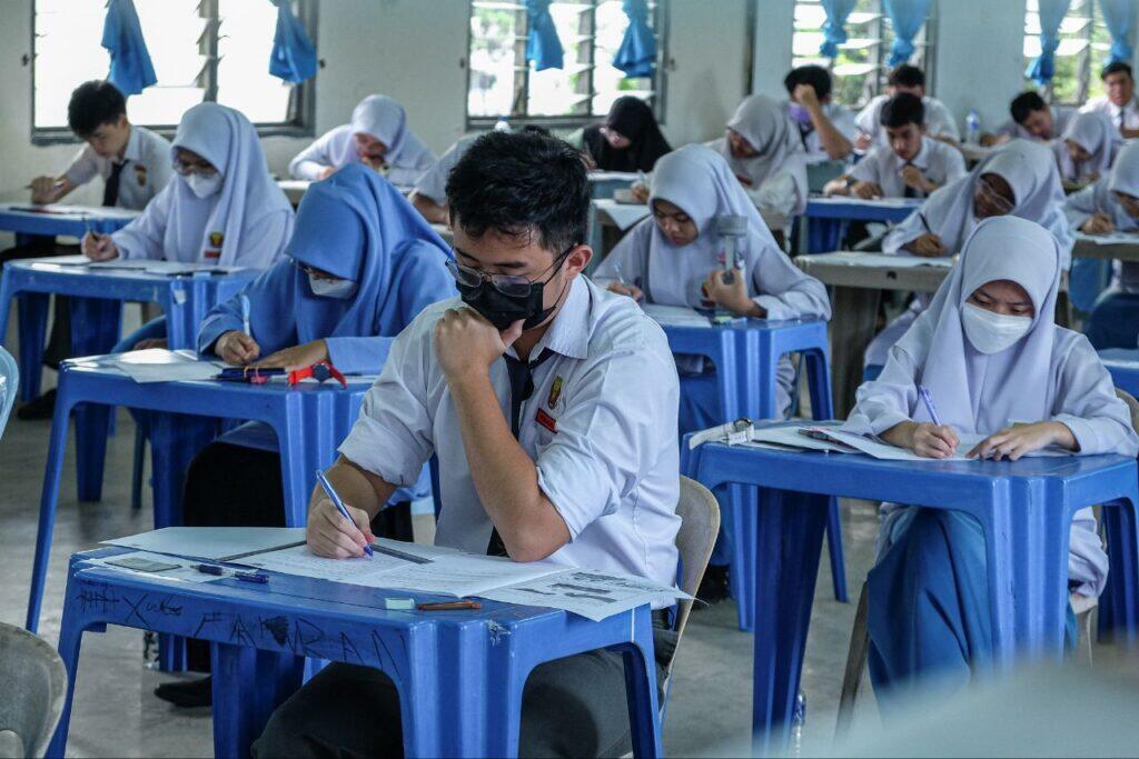 Students taking an exam in blue chairs in an examination hall