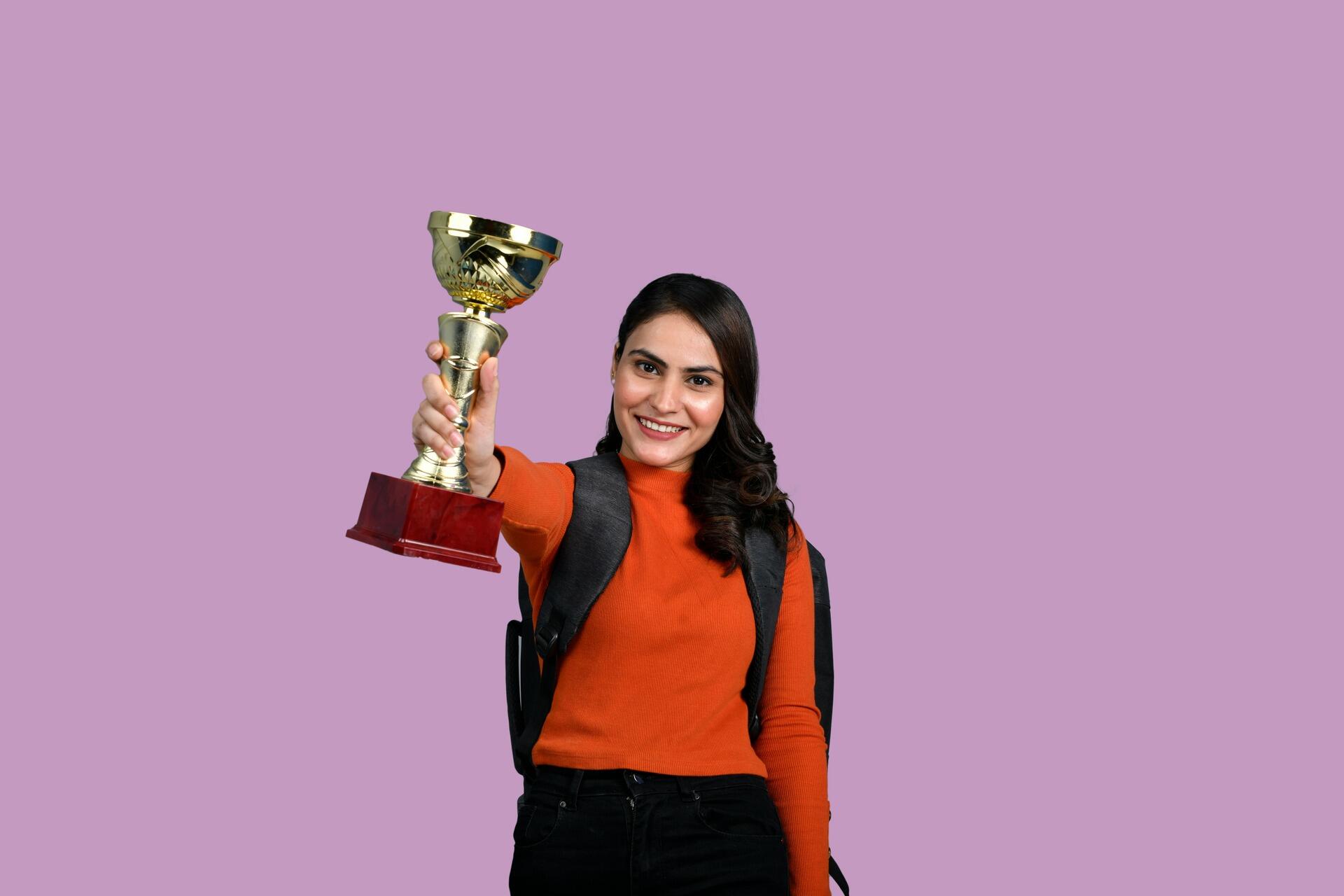 Smiling woman holding a trophy, symbolizing achievement through consistent effort