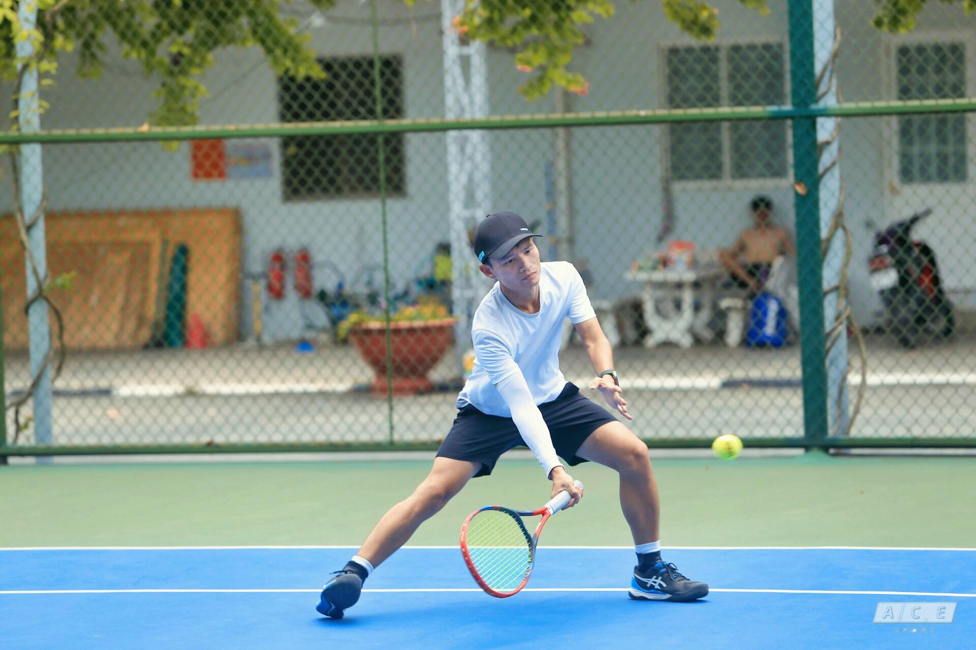 Male tennis player in a white shirt and cap hitting a low backhand shot on a blue and green tennis court.