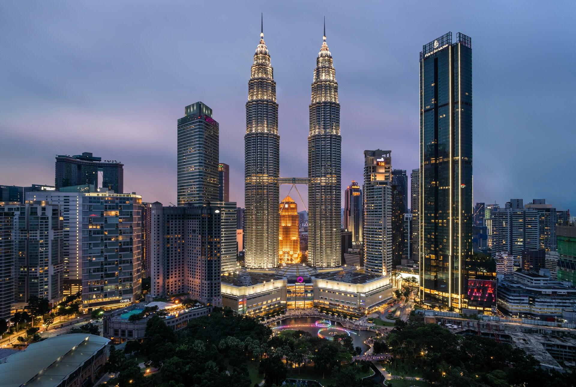 Kuala Lumpur city skyline at dusk featuring the illuminated Petronas Twin Towers and surrounding skyscrapers.