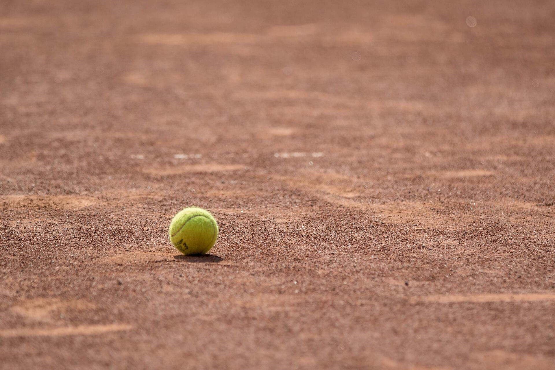 Yellow tennis ball sitting on a clay court surface.