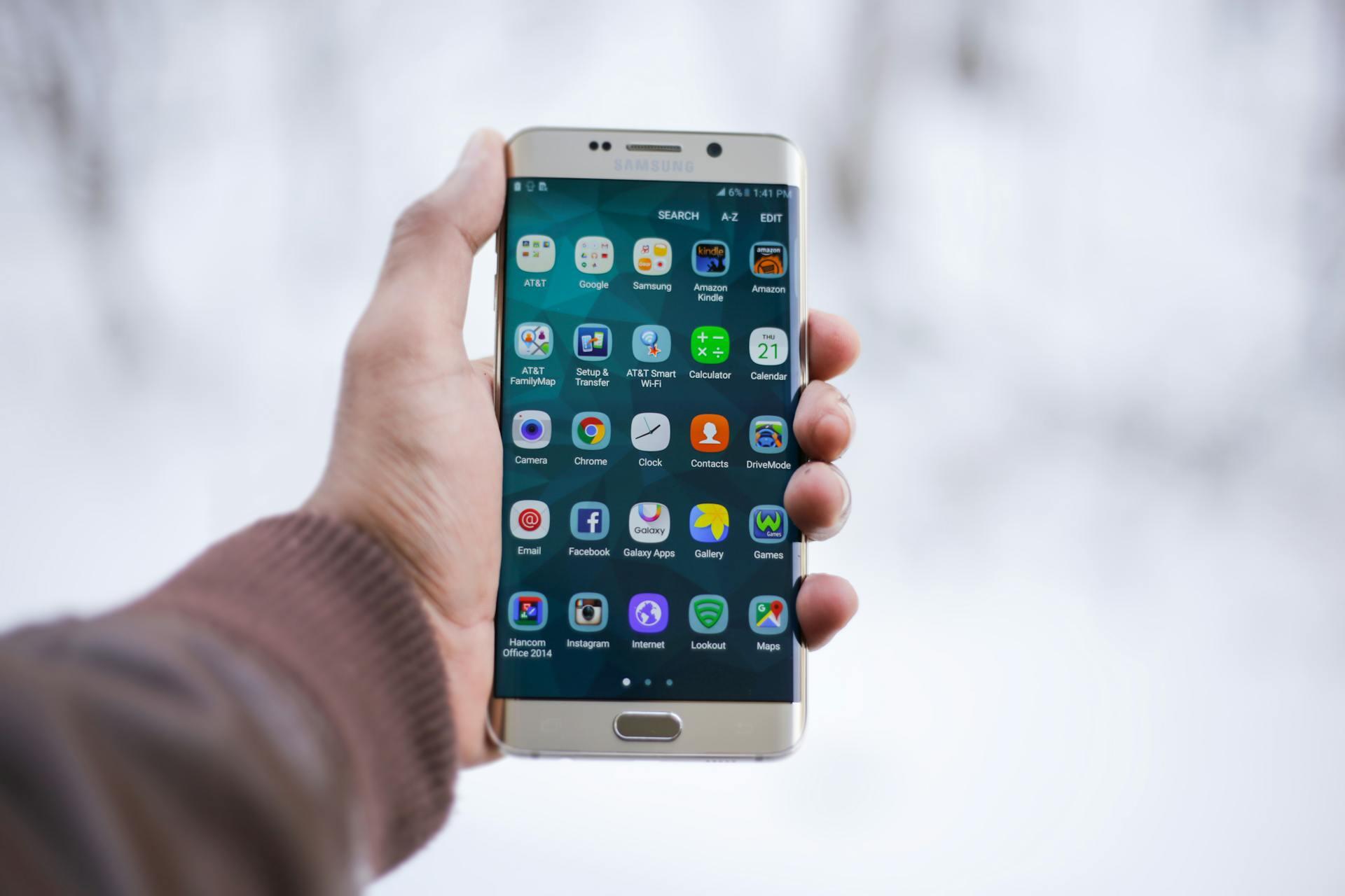 Hand holding a smartphone displaying the home screen with various mobile apps arranged in a grid layout.