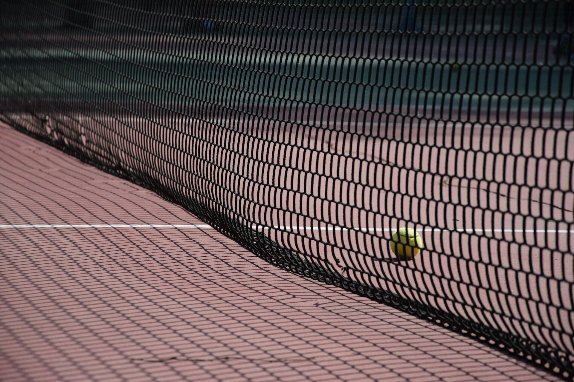 Tennis net casting shadows on a clay court surface.
