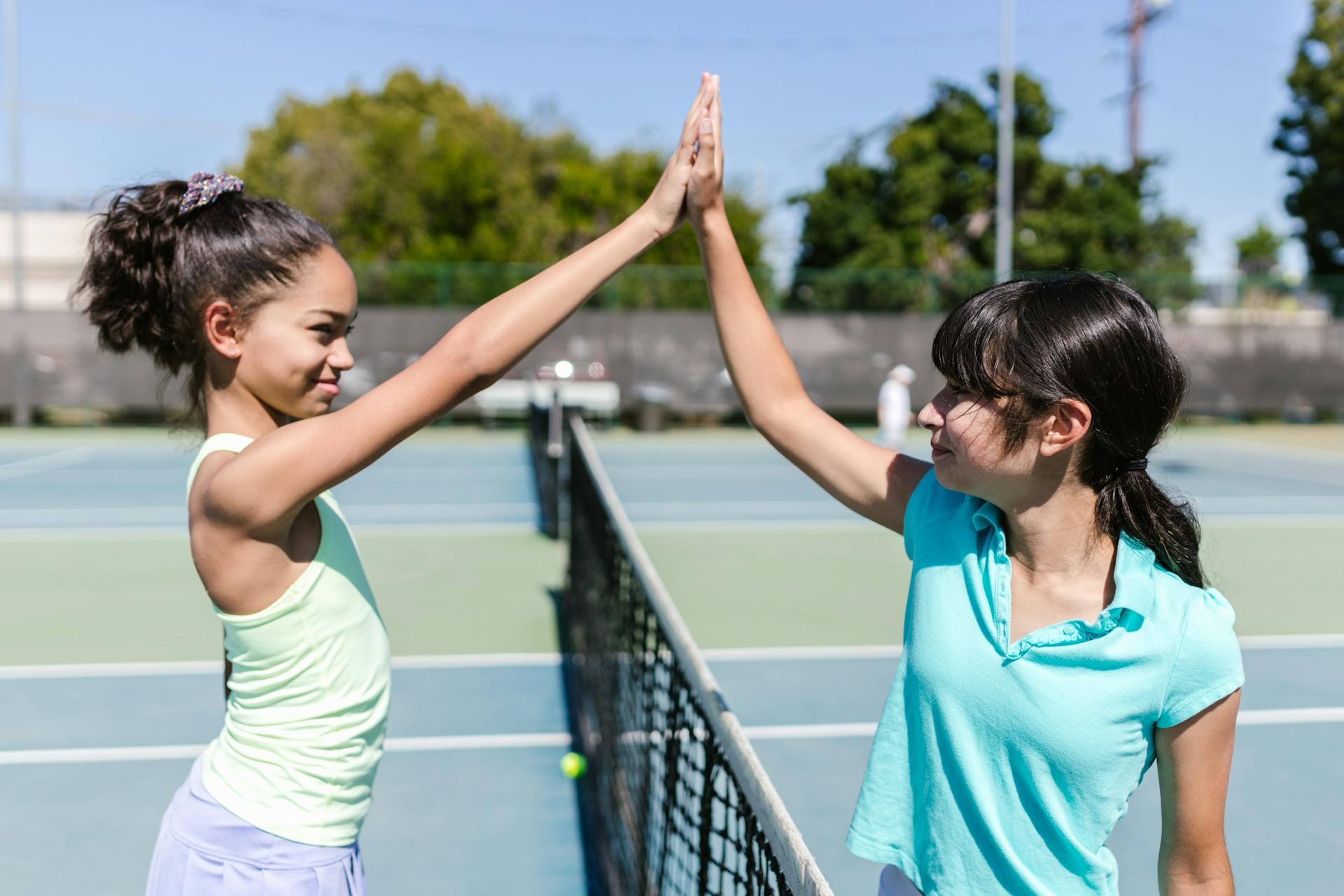 Two young women giving each other a high-five on a tennis court after playing a match.