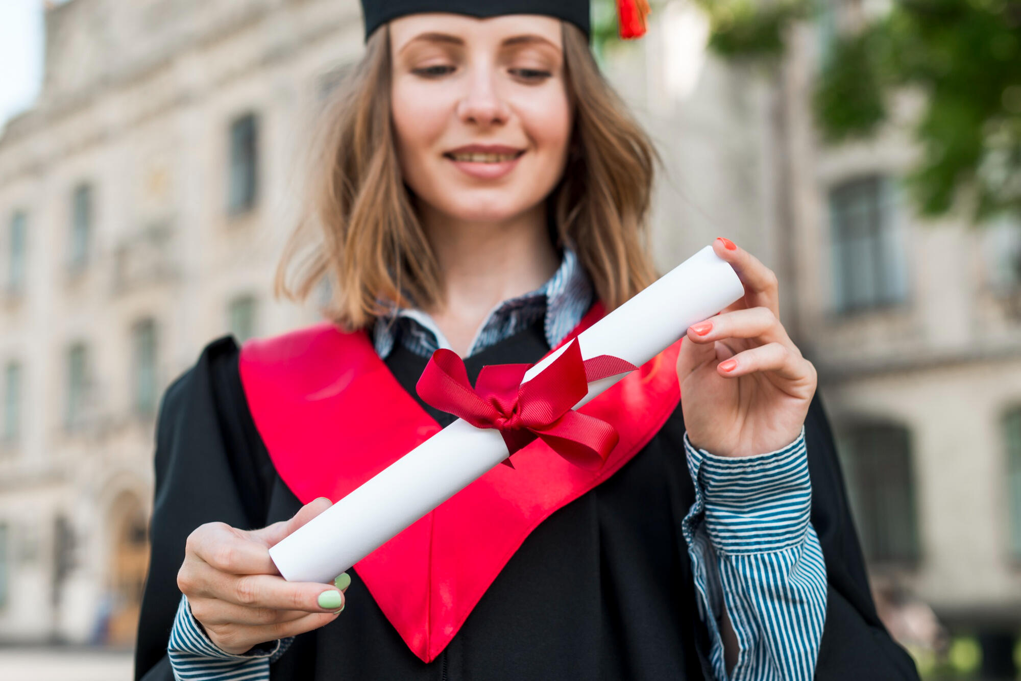 A woman in a graduation gown proudly holds her diploma, celebrating her academic achievement.