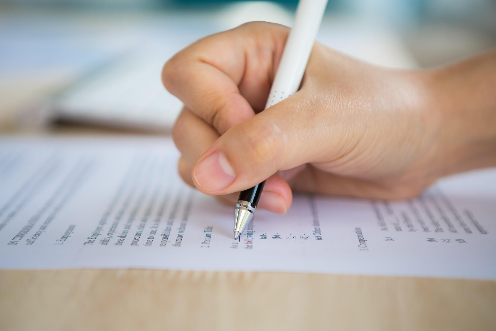 A close-up of a hand holding a pen, writing on a sheet of paper.