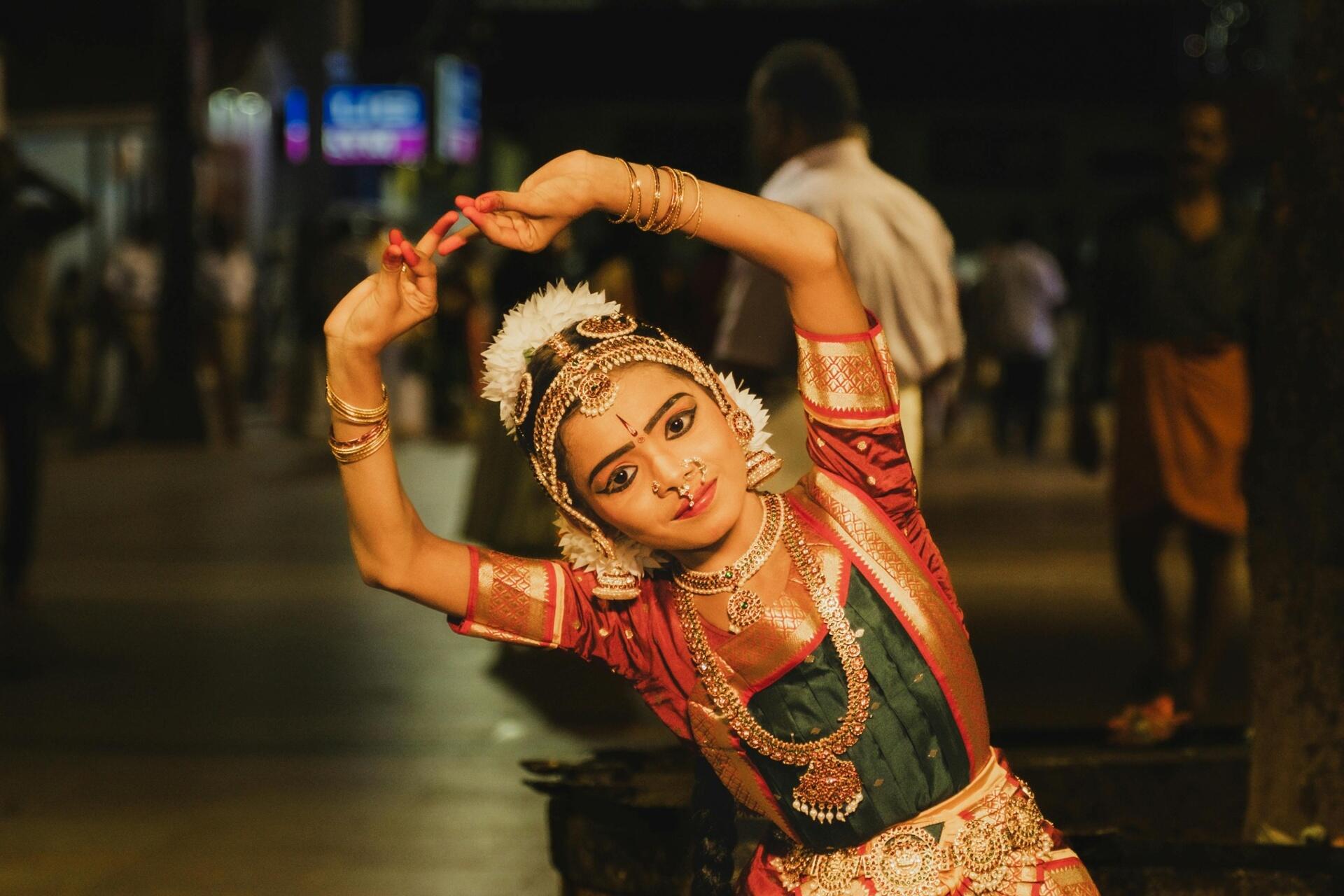 Bharatanatyam dancer performing a traditional Tamil classical dance pose in elaborate costume and temple jewellery at night.