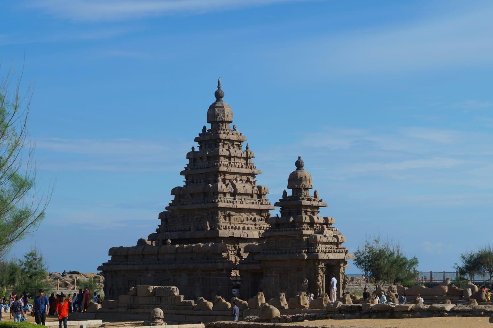 Ancient stone Hindu temple with Dravidian architecture under a bright blue sky near the coast.