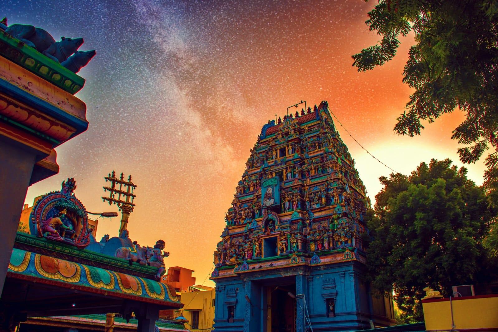 Colourful Hindu temple with detailed Dravidian gopuram under a dramatic starry evening sky.