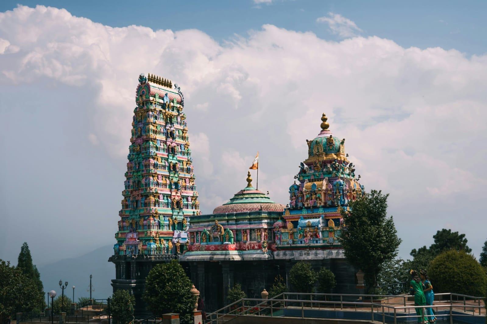 Colourful Hindu temple with ornate Dravidian architecture and towering gopuram under a cloudy blue sky.