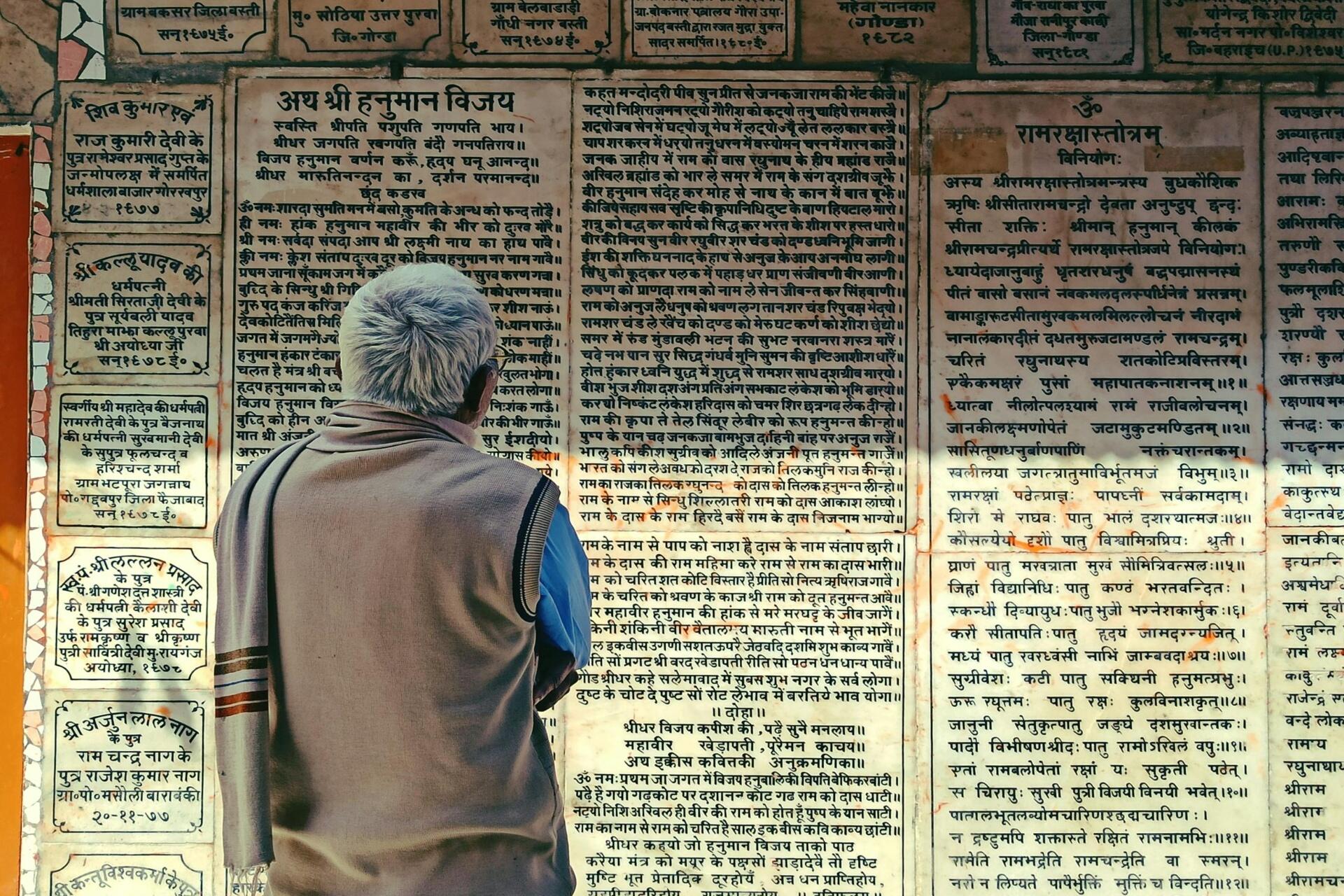 Person standing in front of a wall covered with Hindi and Sanskrit script inscriptions, reading the engraved text in a heritage setting.