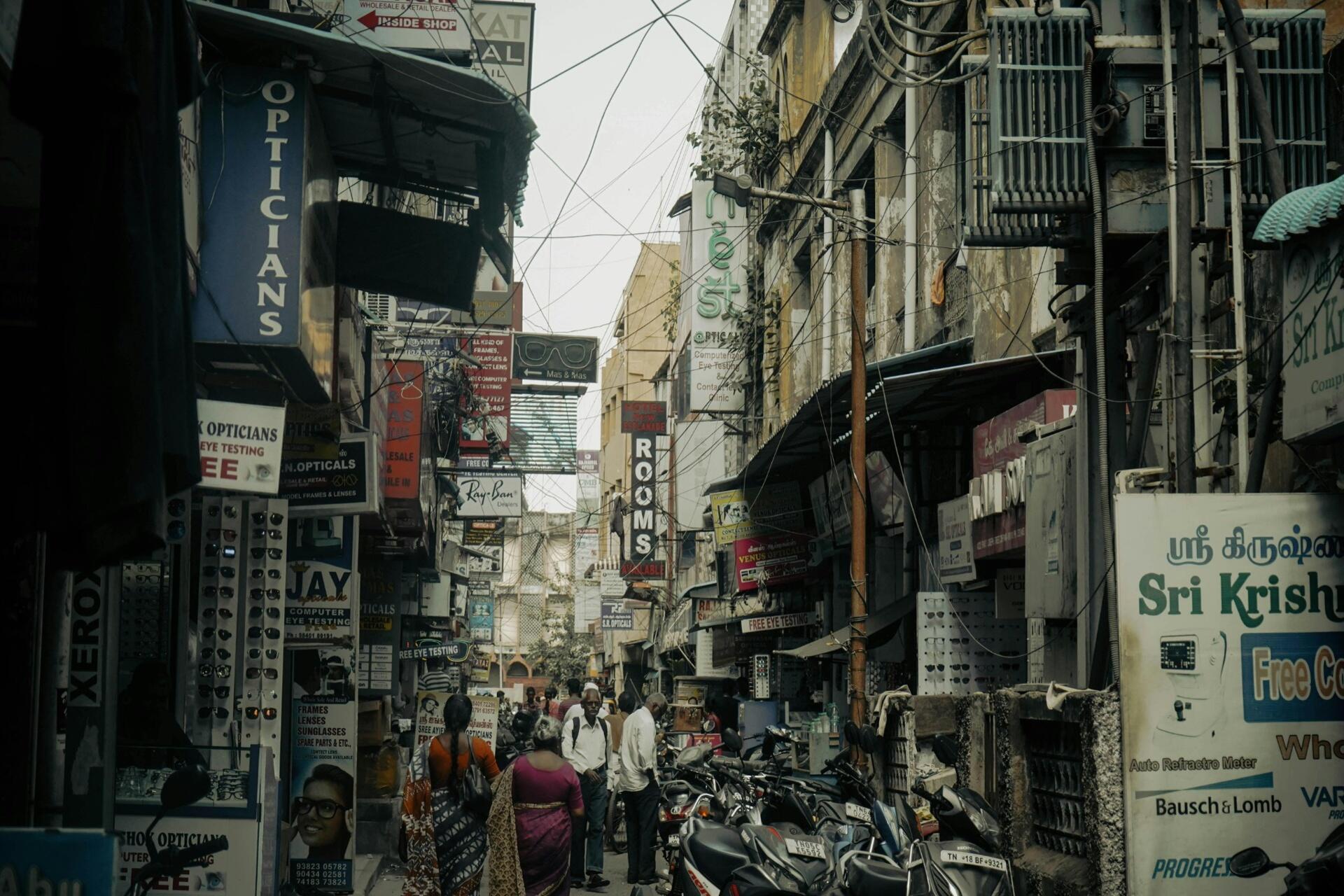 Busy street market with Tamil signboards, shops, and pedestrians in an urban Indian setting