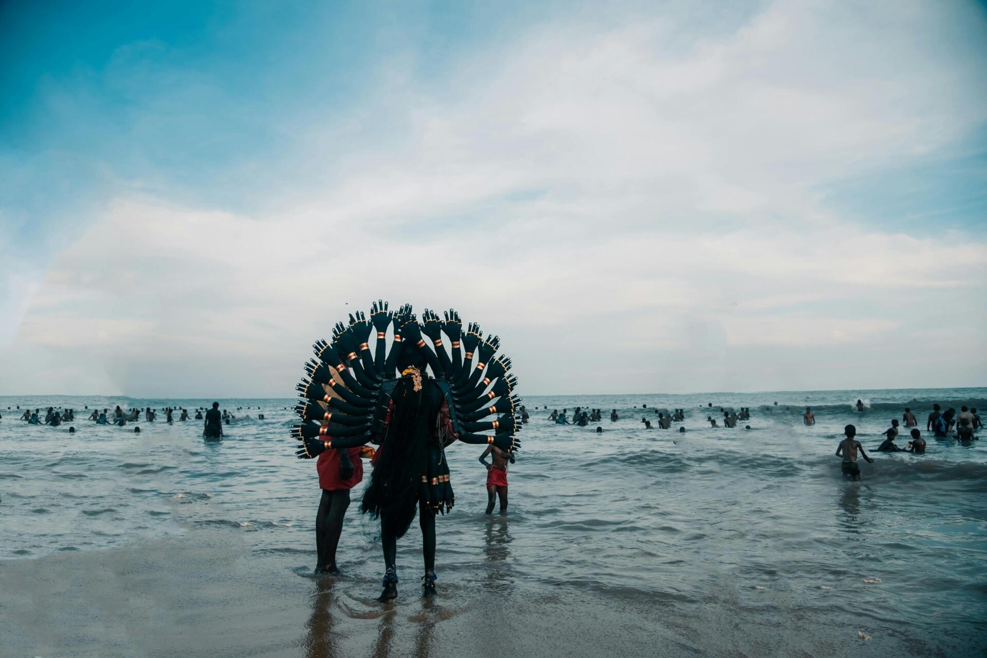 Participant in traditional Tamil religious festival attire standing by the sea during a cultural devotional gathering
