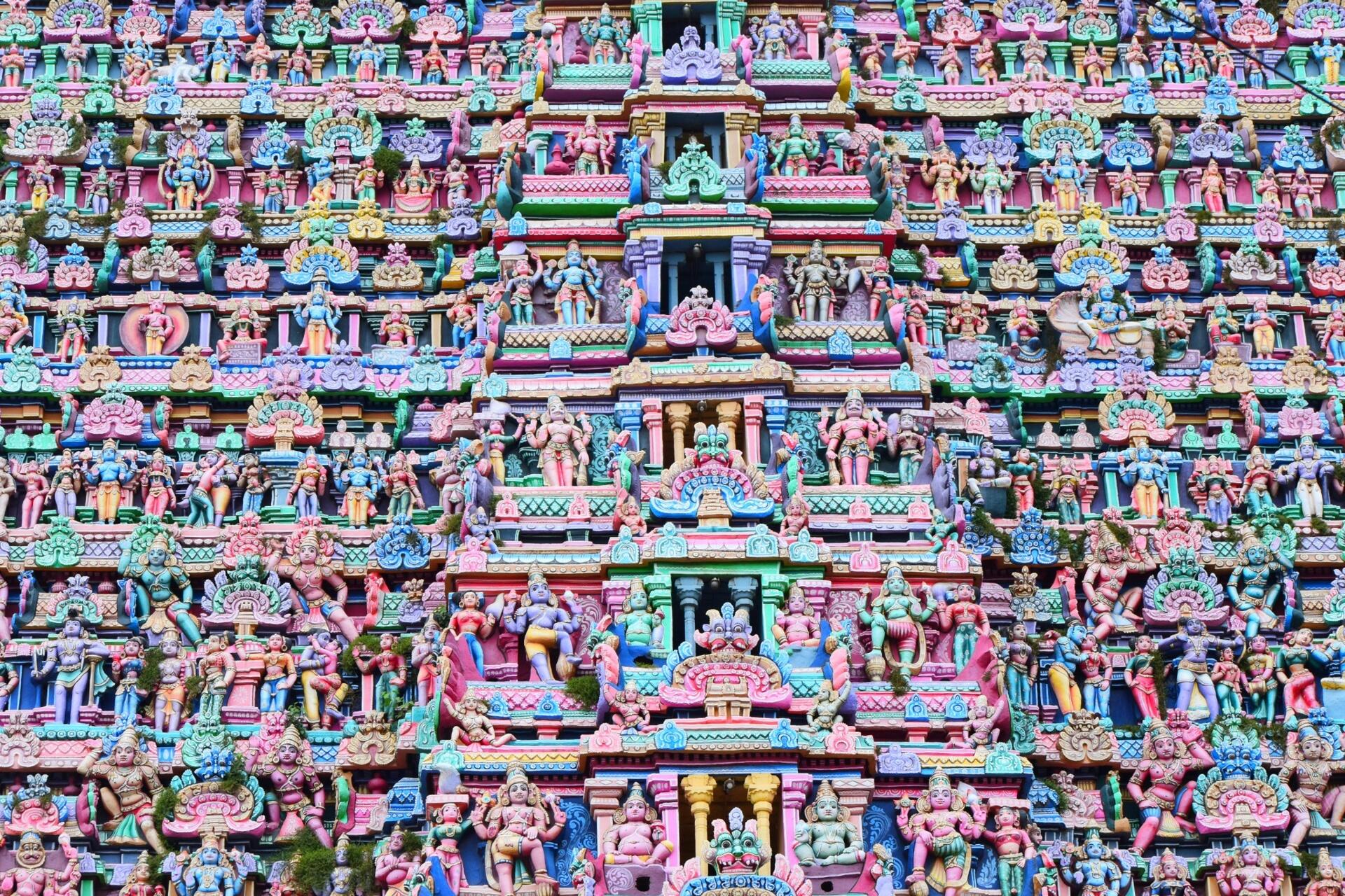 Colourful close-up of a South Indian temple gopuram featuring intricate sculpted deities and decorative Dravidian architectural details.