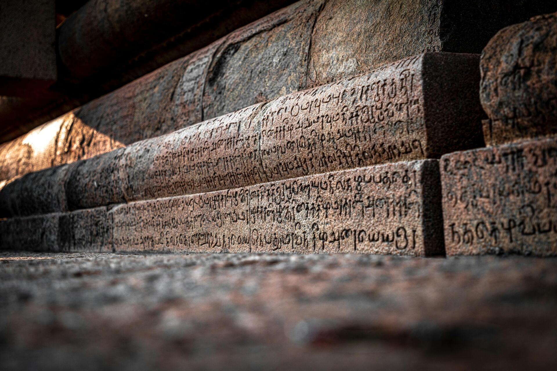 Ancient Tamil stone inscriptions carved across temple steps, showing historic Tamil script engraved in weathered stone.