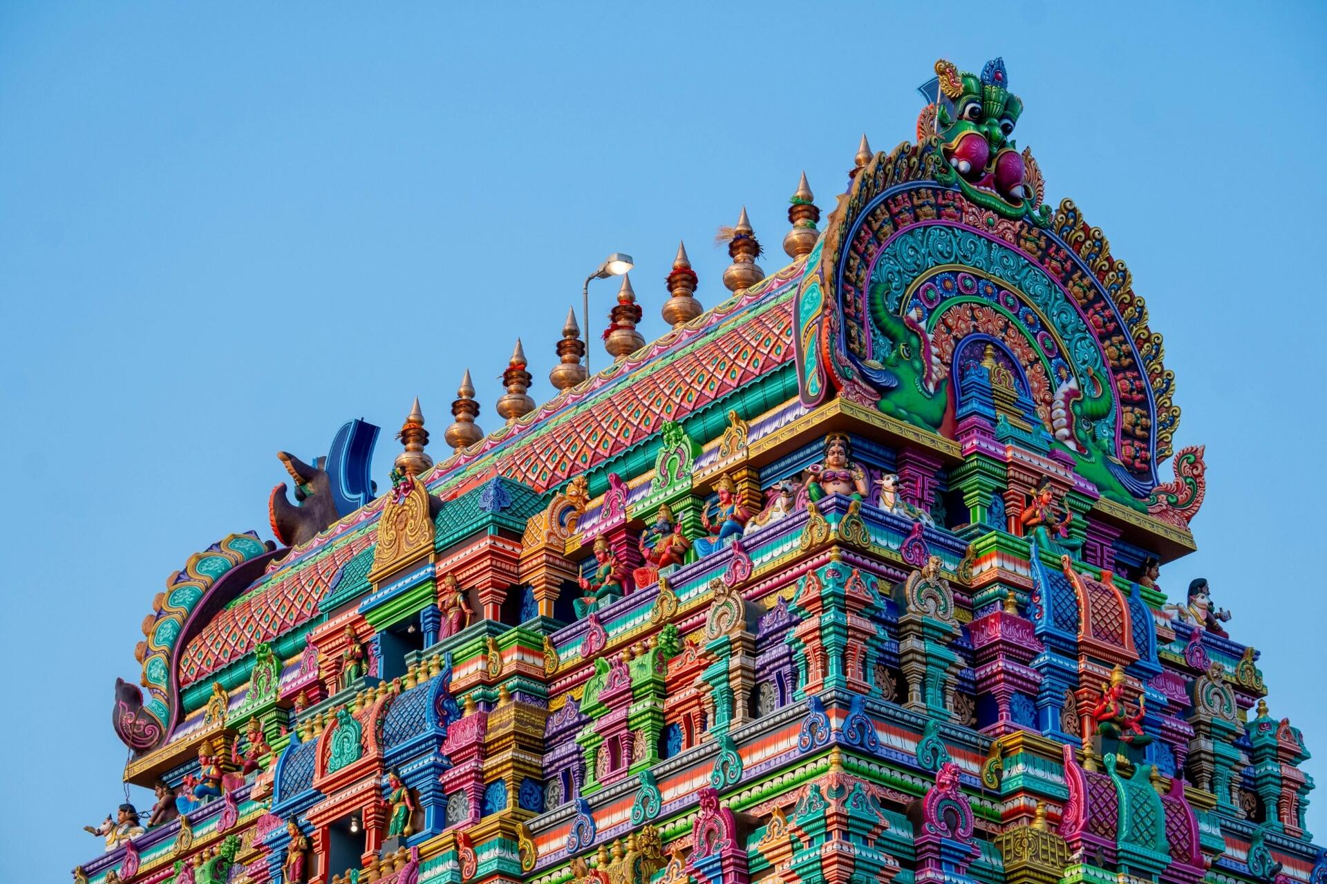 Colourful South Indian temple tower featuring ornate Dravidian architectural carvings and decorative sculptural details against a clear blue sky.