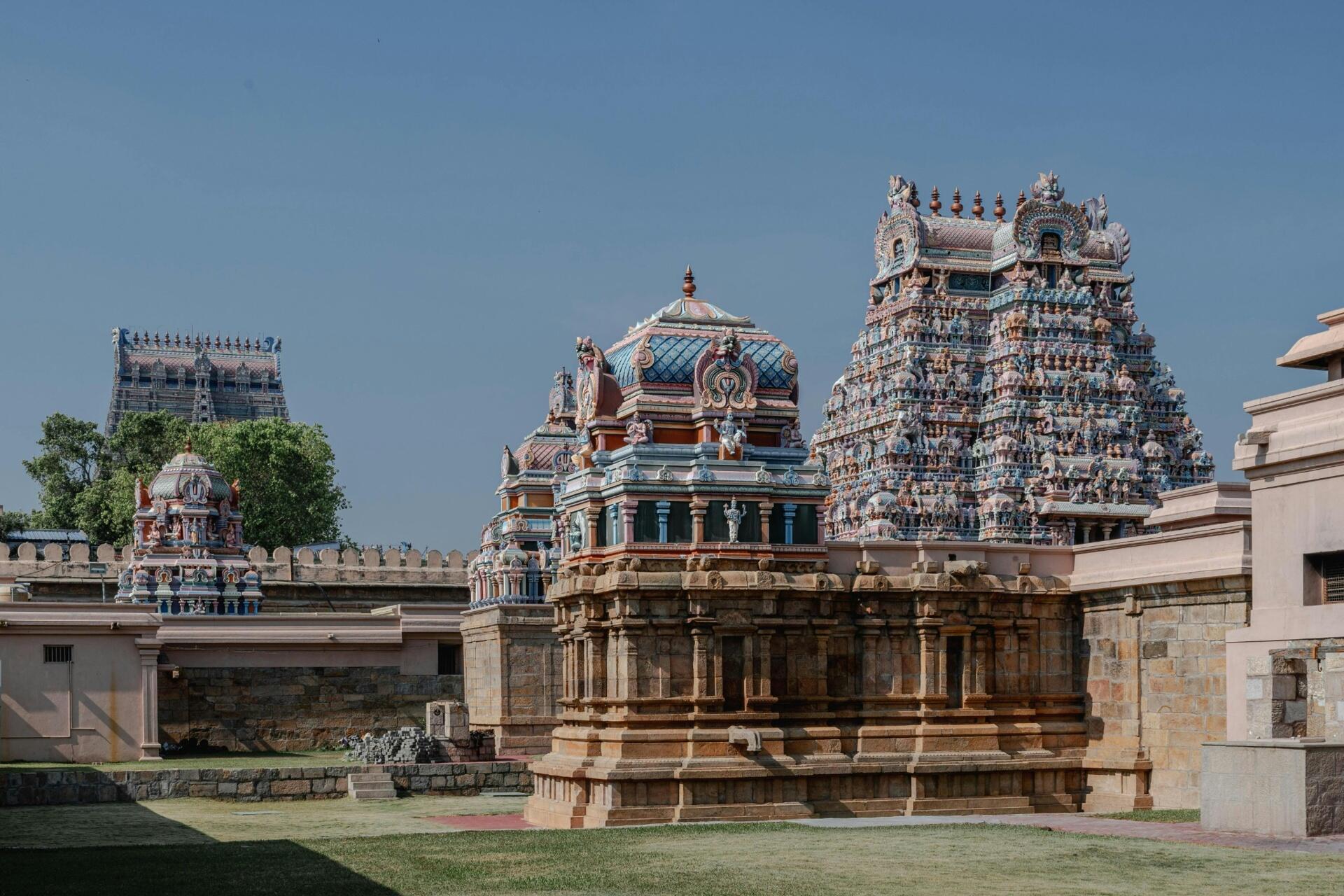 Historic South Indian temple complex featuring colourful Dravidian-style towers, ornate carvings, and traditional Tamil architectural elements under a clear blue sky.