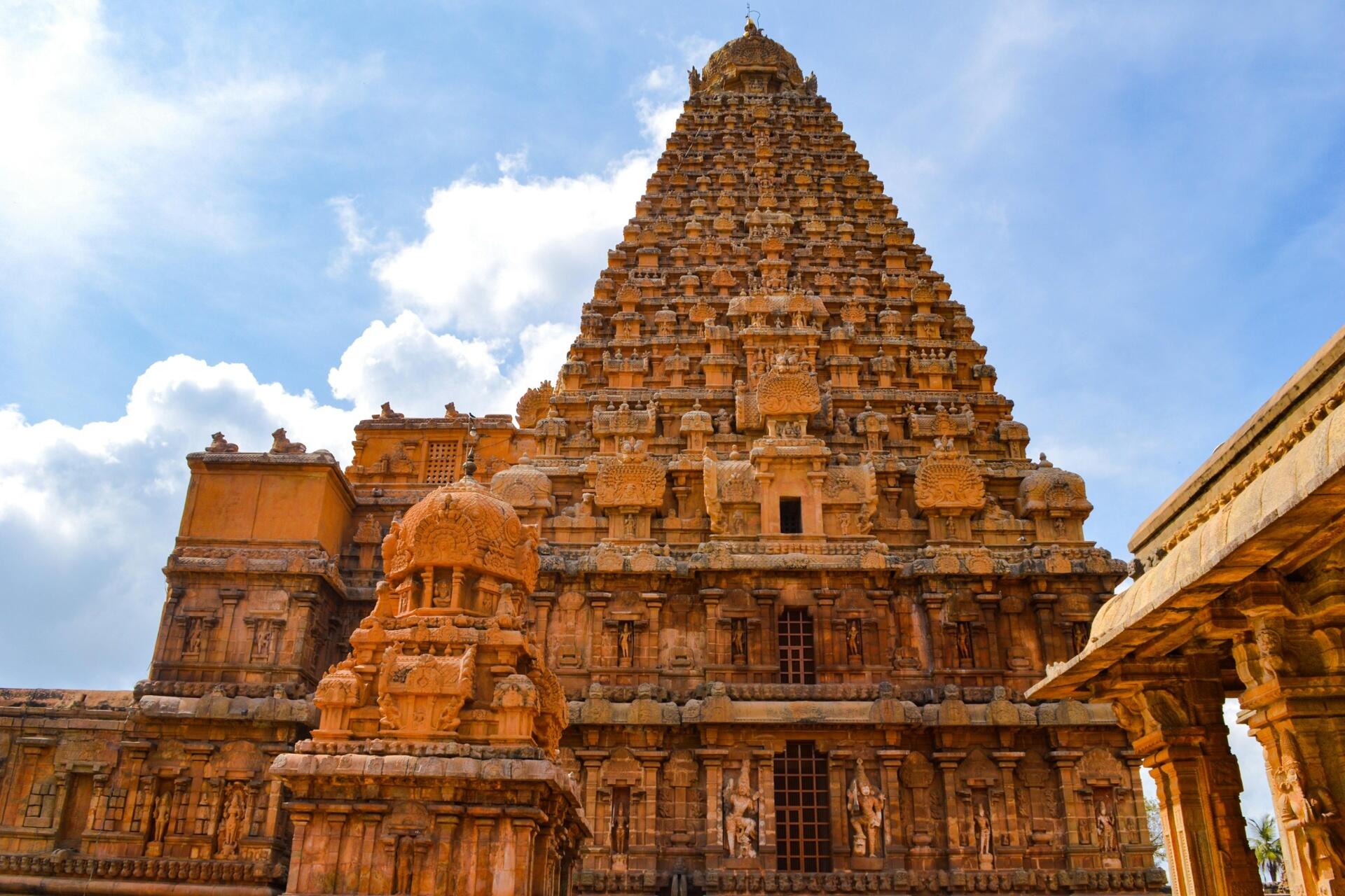 Historic South Indian temple with intricate Dravidian architecture and a towering stone vimana under a bright blue sky.