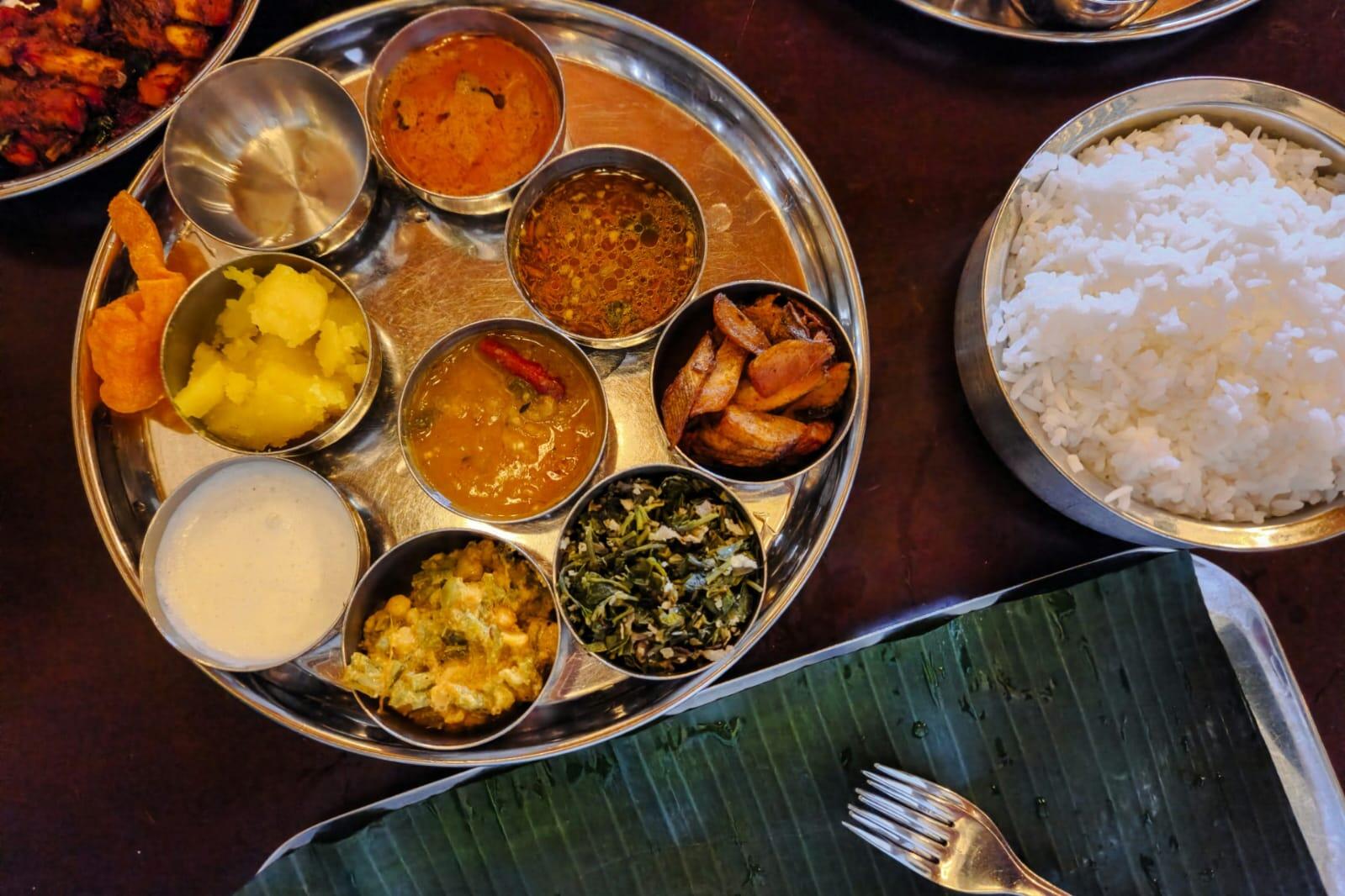 Traditional South Indian thali meal with rice, curries, vegetables, and banana leaf on a dining table.