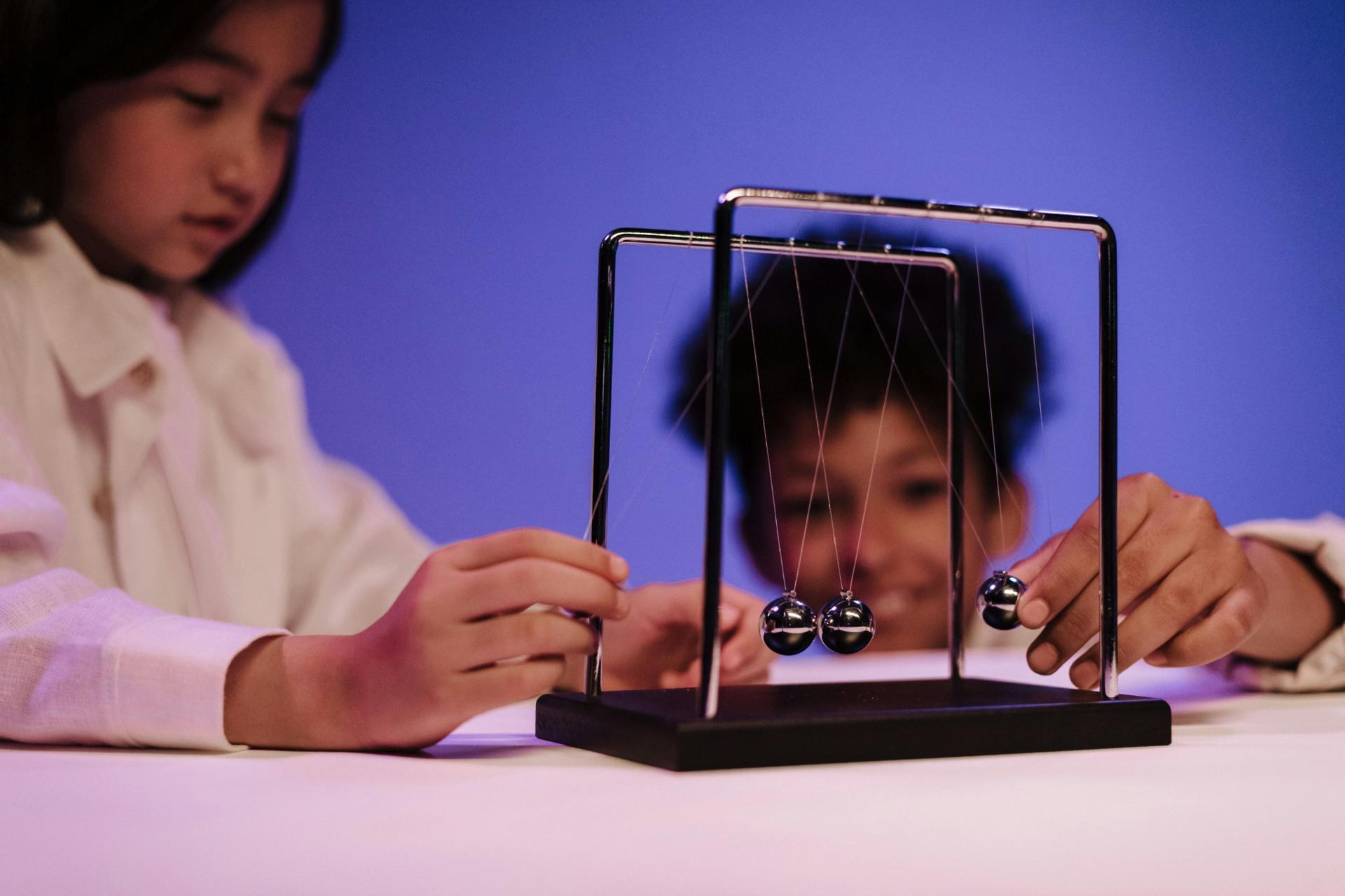 Students interacting with a Newton cradle demonstrating motion, momentum, and energy transfer in physics
