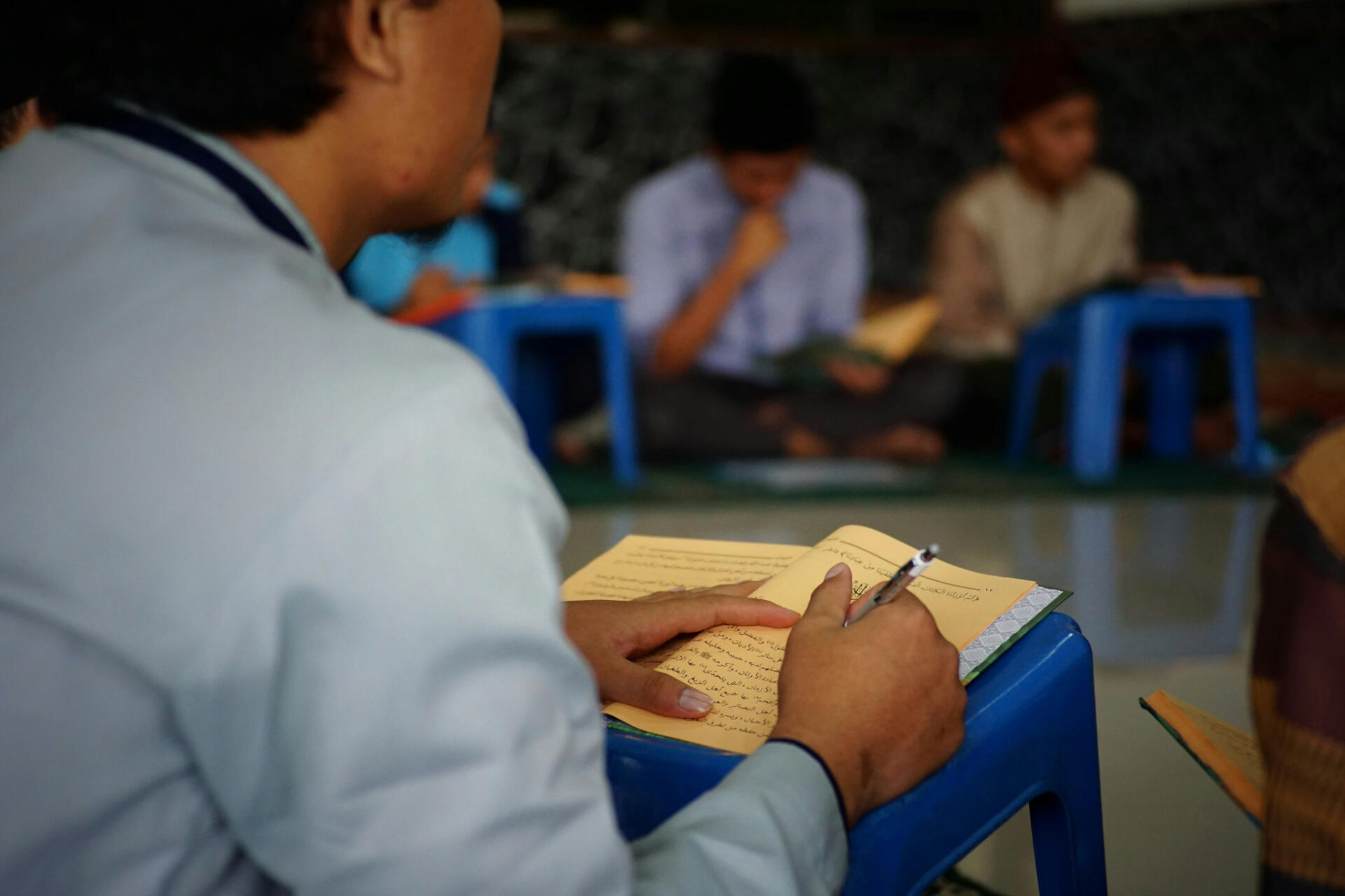 Students sitting on the floor with small tables, studying texts and taking notes during a classroom session.