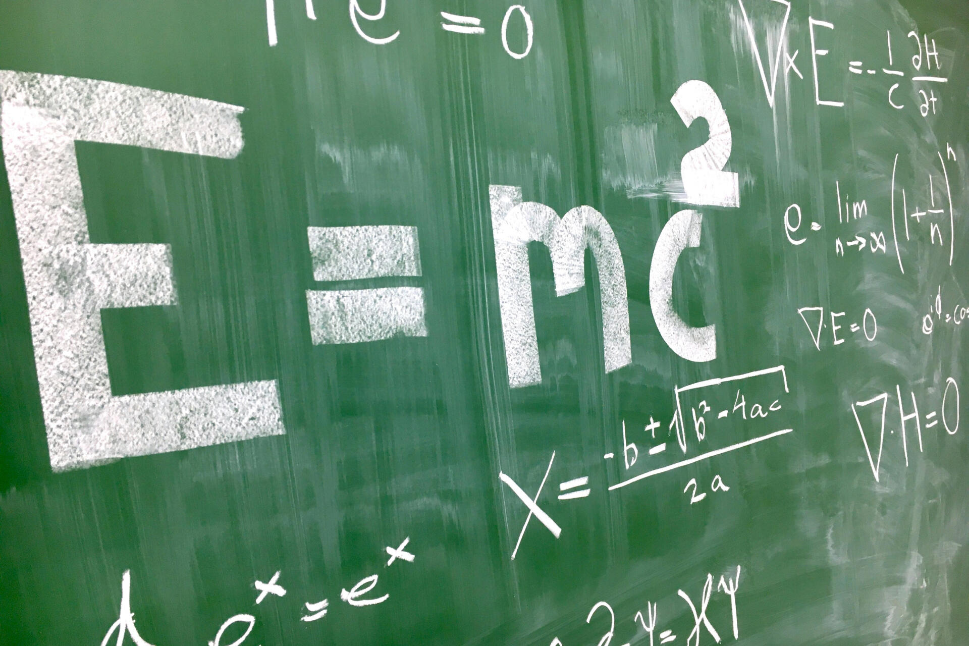 Chalkboard filled with famous mathematical and physics equations including Einstein’s E=mc² and the quadratic formula.