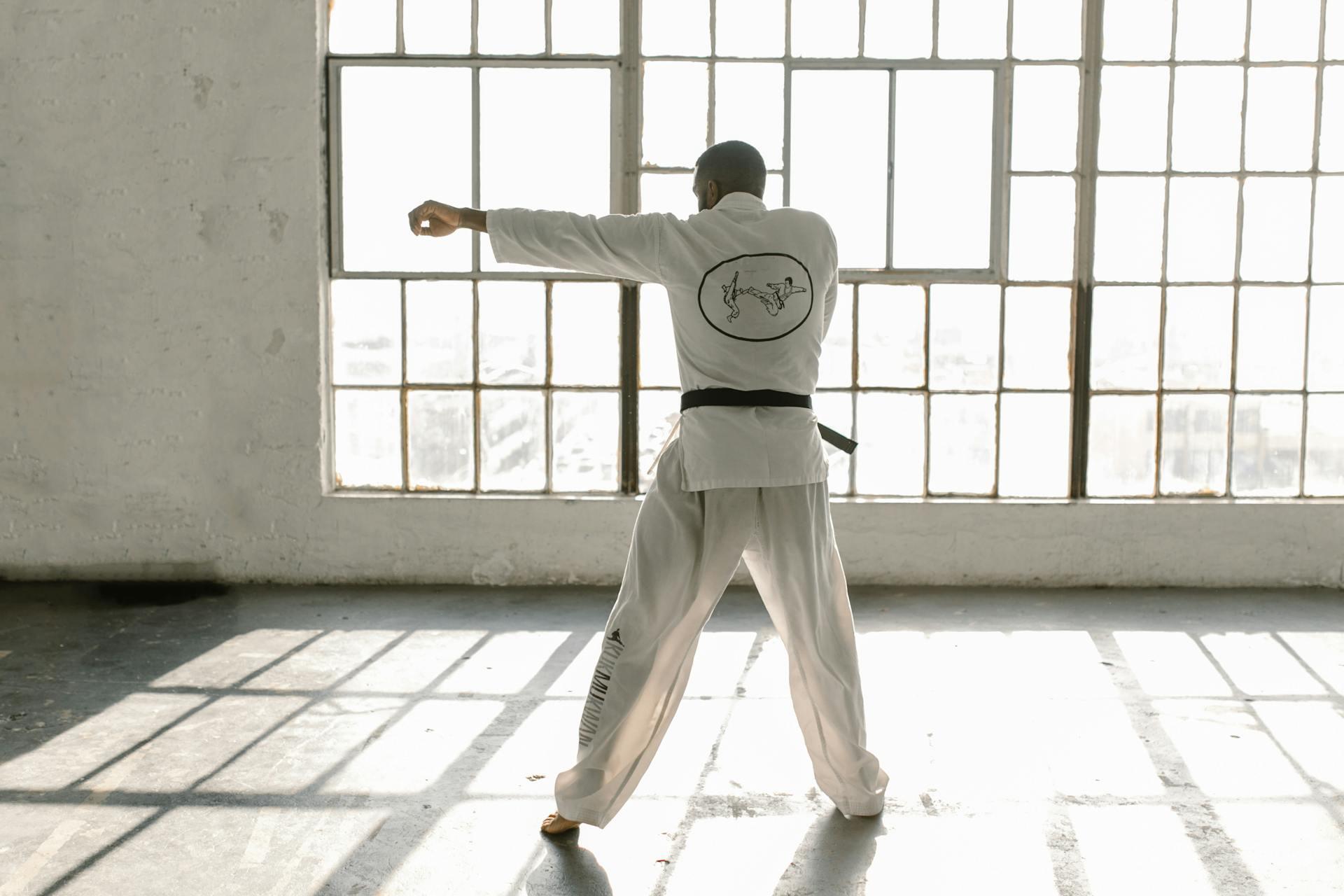 A man in a white shirt and black belt is practising karate in a dojo setting.