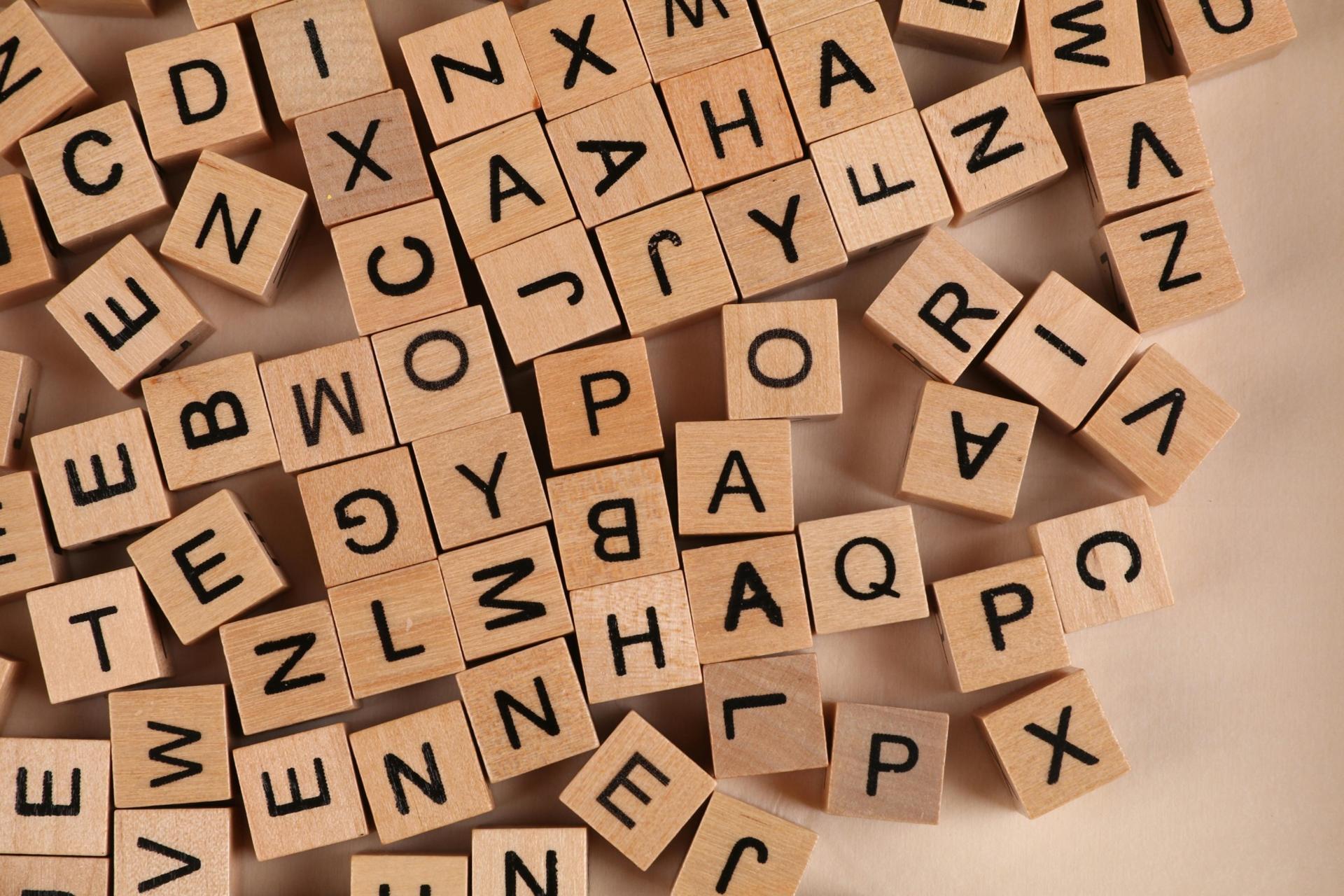 Wooden letter tiles scattered across a surface representing vocabulary building, language learning, and preparation for the UEC English examination.