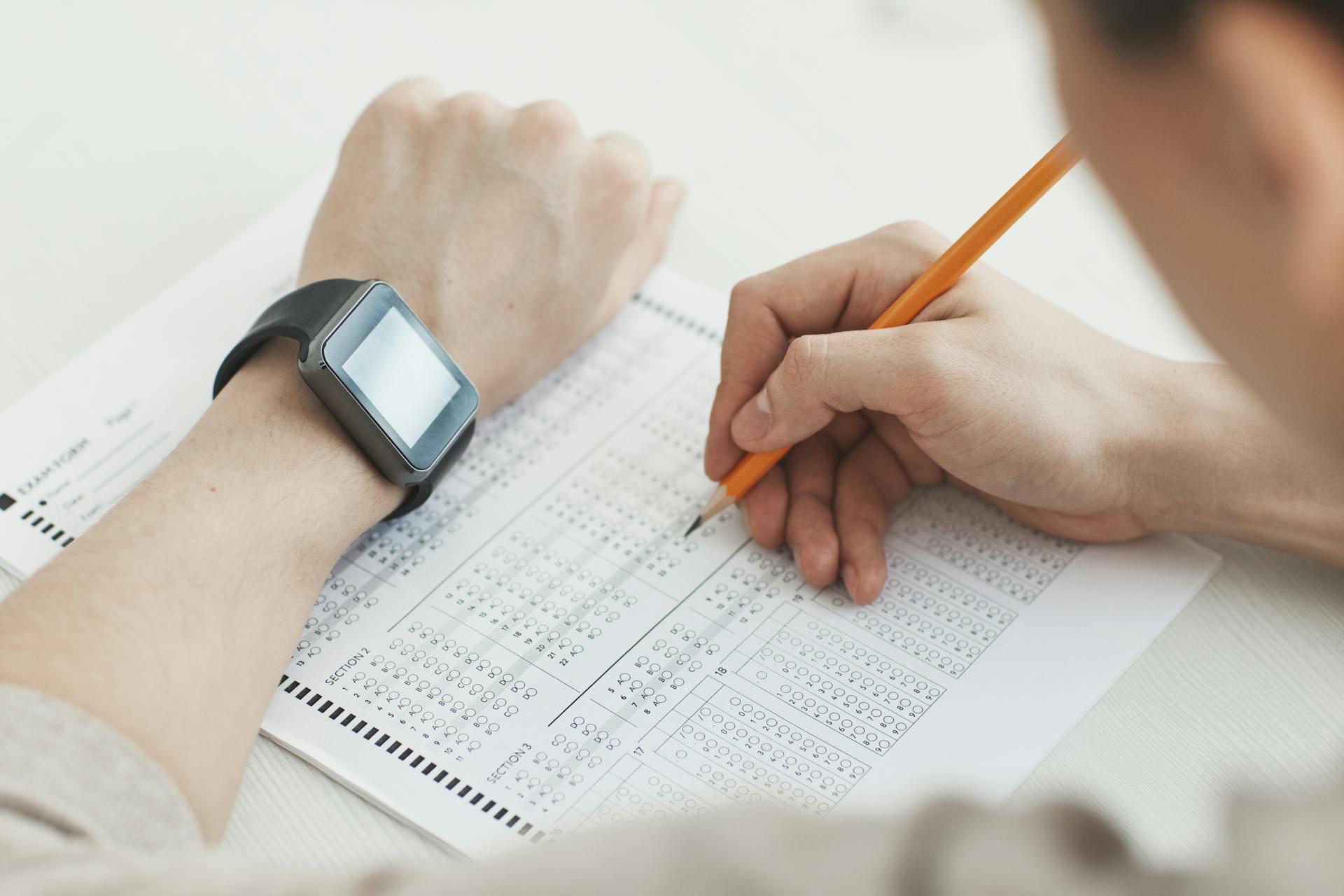 A student focused on an exam, wearing a smartwatch on their wrist, surrounded by exam papers and a pencil.