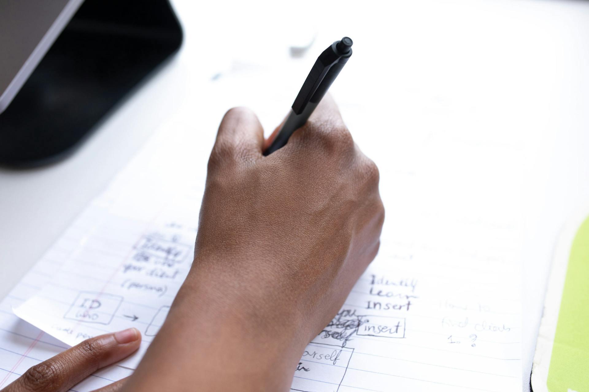 A person writing with a pen on a piece of paper, focused on their task in a well-lit environment.