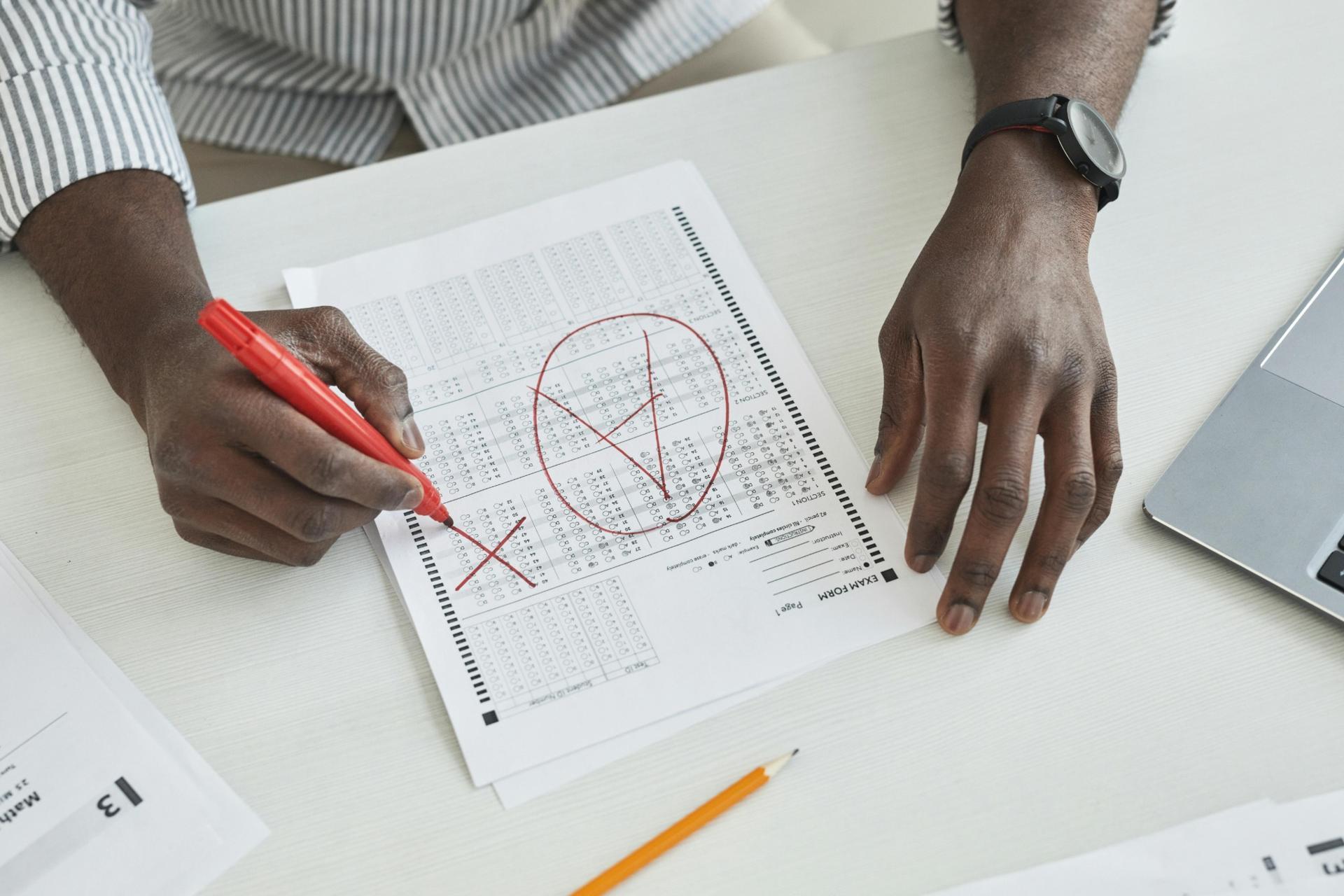 teacher marking exam paper with red pen highlighting mistakes on answer sheet