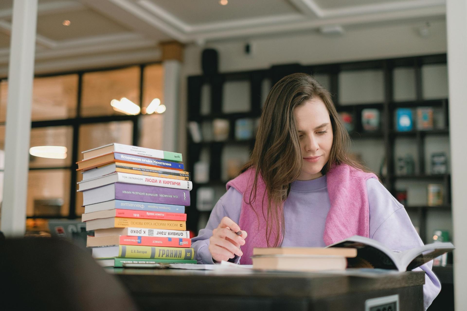 student studying with stack of books reading and taking notes for exam preparation