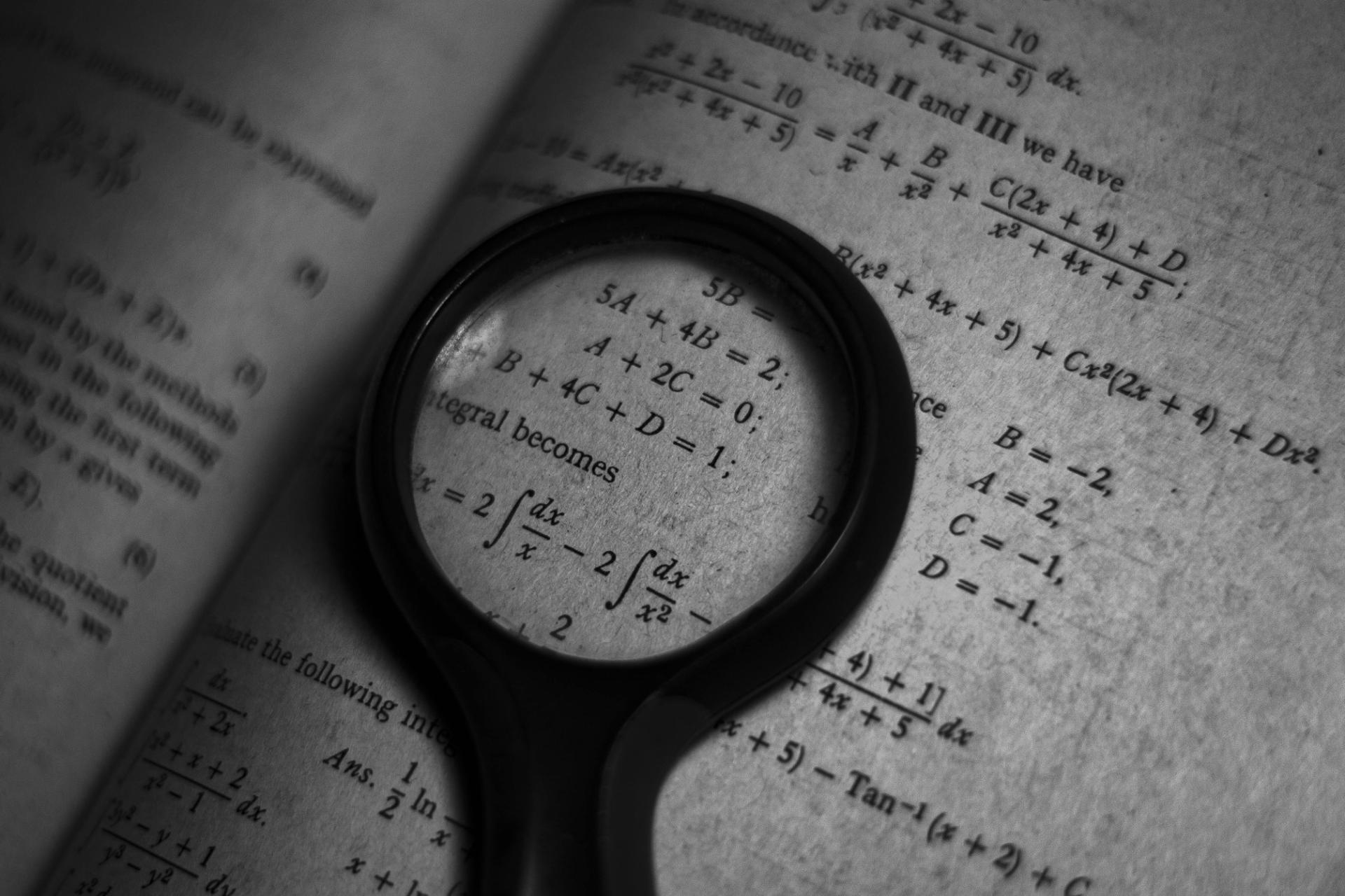 Close-up of a mathematics textbook with equations viewed through a magnifying glass