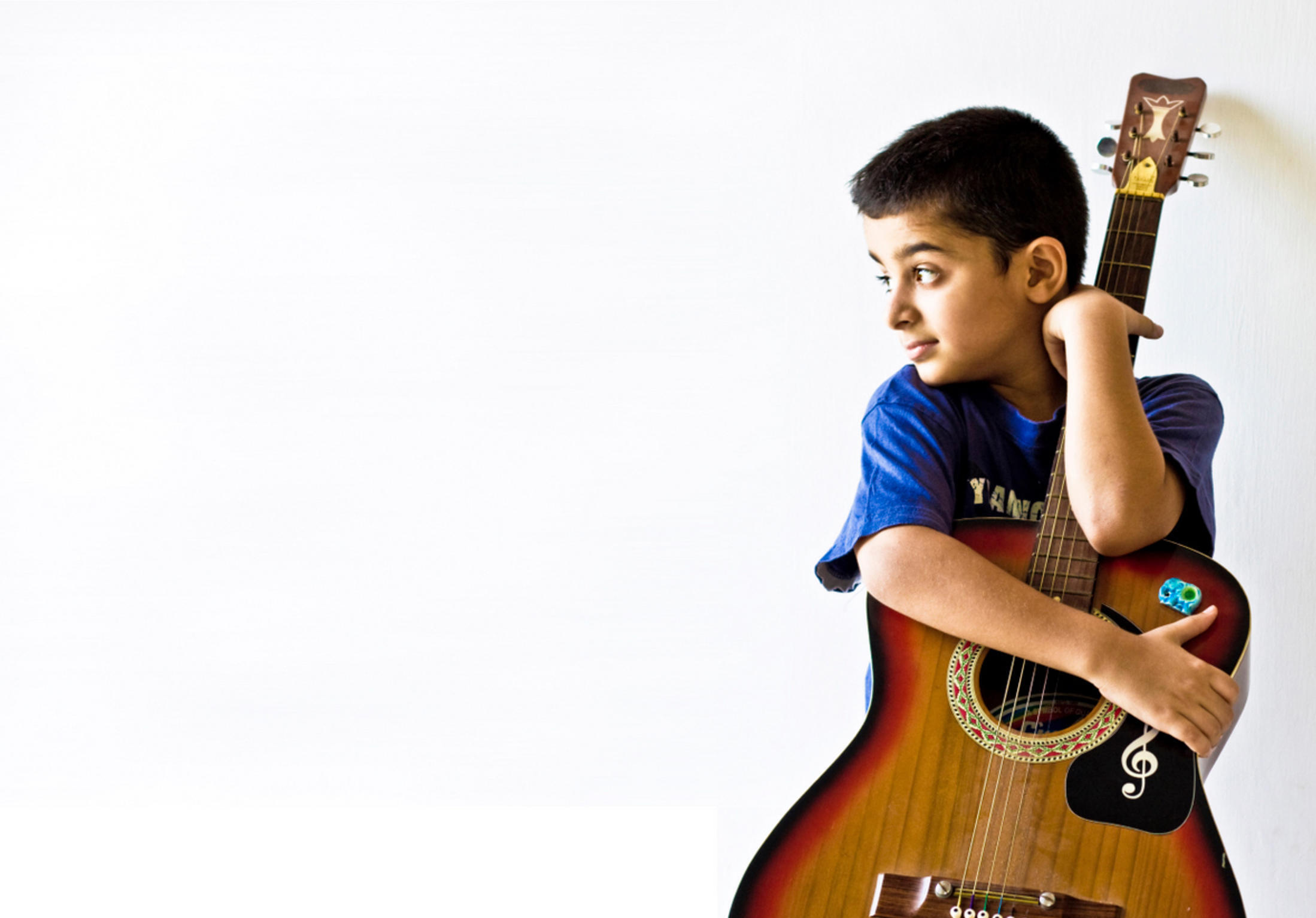 Boy holding a guitar against a white background.