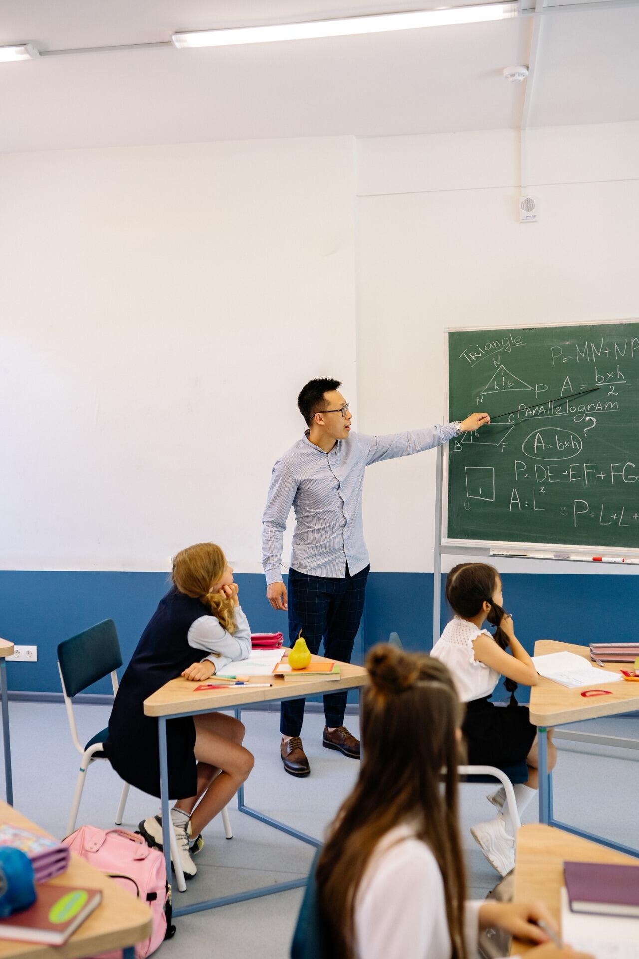 Mathematics teacher explaining geometry formulas to students during a classroom lesson.