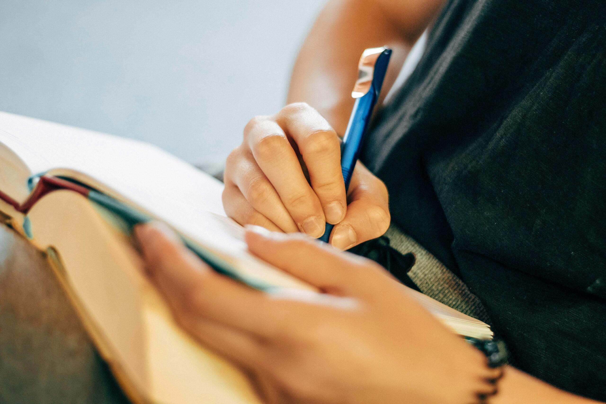 A person writing notes in their book with a blue pen.