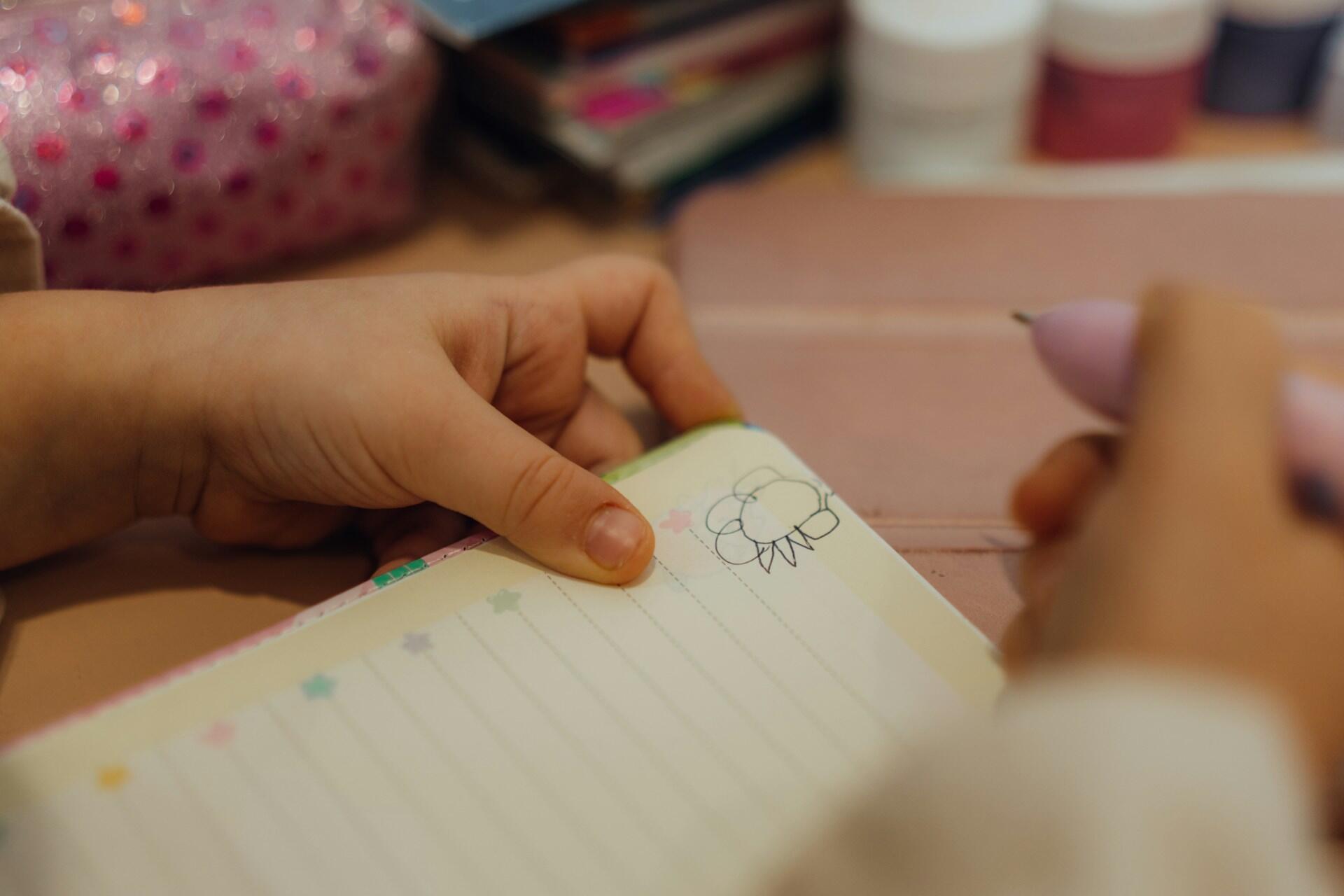 A student writing revision notes in a notebook with a pen.