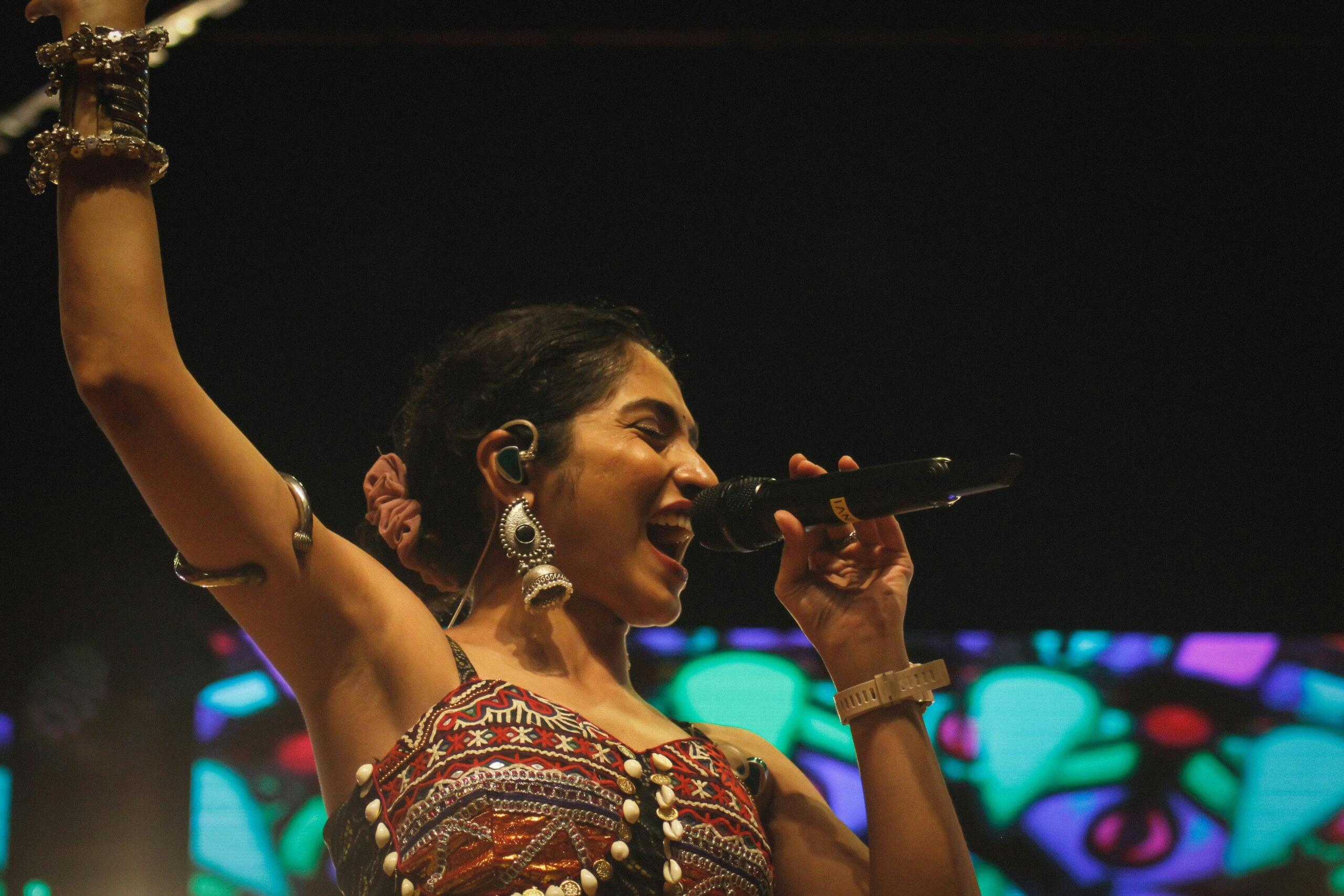 A woman in a vibrant dress passionately singing into a microphone on stage.