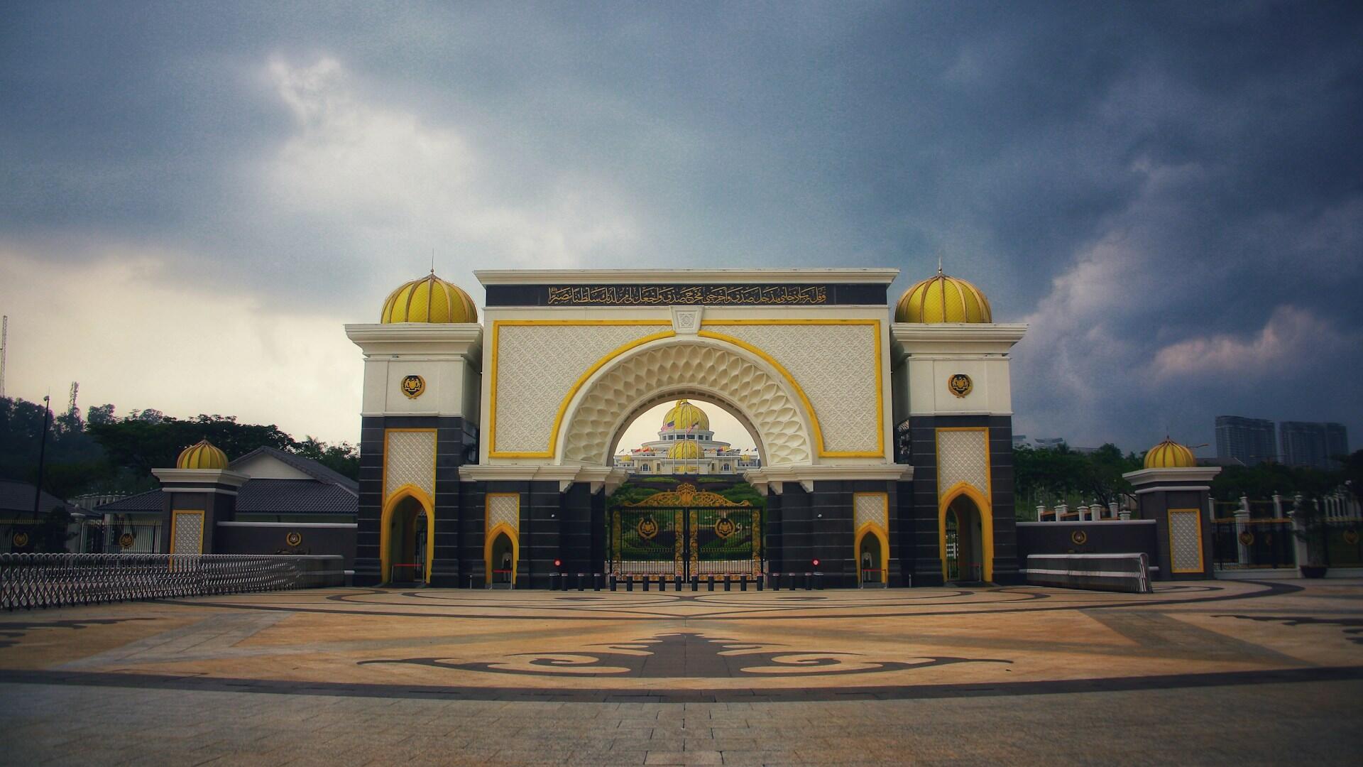 Grand entrance gate of Istana Negara, Malaysia’s National Palace, featuring gold domes and intricate designs under a cloudy sky.
